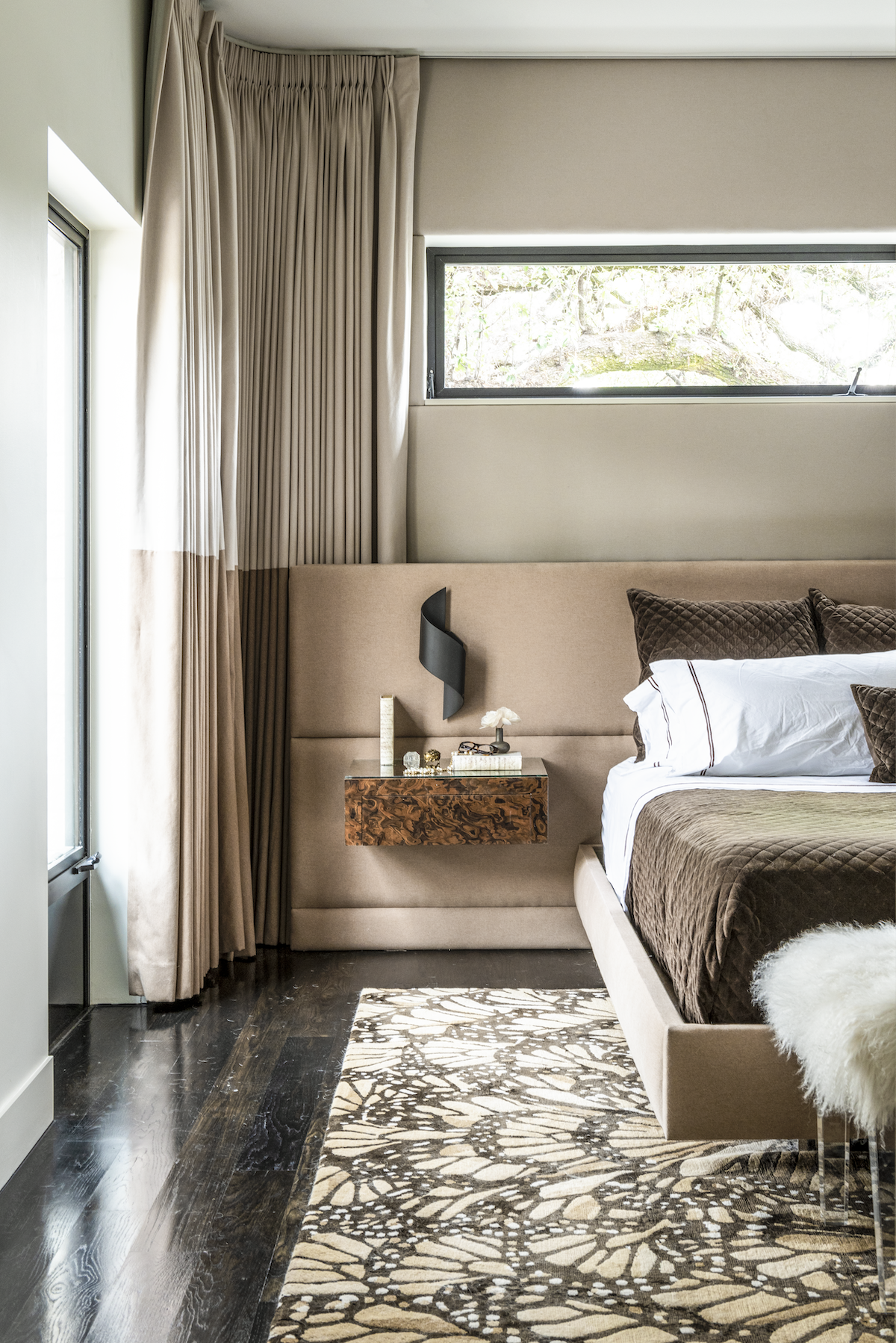 Midtown Manhattan bedroom with upholstered wall panels, layered neutral textiles, custom drapery and dark wood flooring.