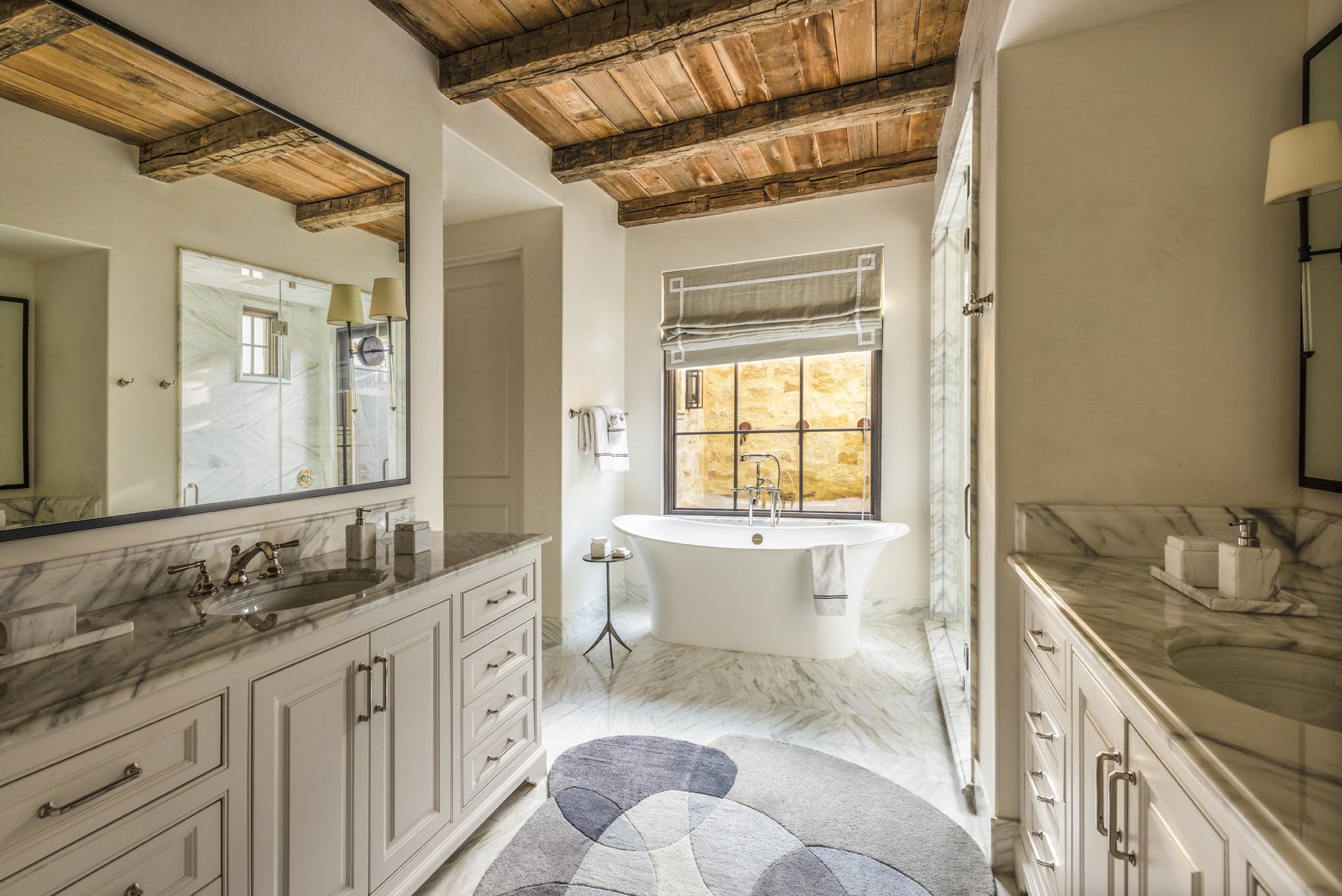 Luxury ranch bathroom with a freestanding tub, marble vanity and flooring, glass shower and reclaimed wood ceiling beams.
