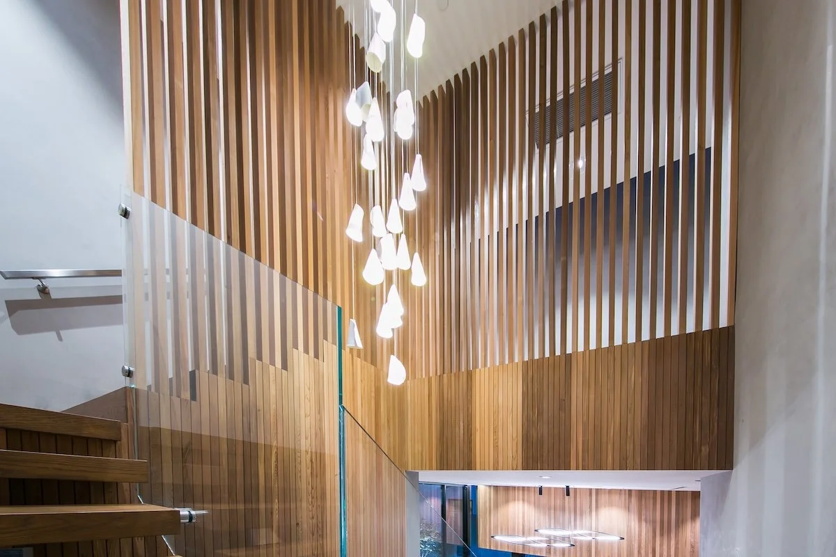 Modern office interior in Midtown Houston with double-height wood slat walls, pendant lighting, and sculptural stair detailing.