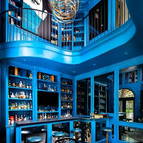 Bold blue bar and lounge interior showing branded hospitality interior design with custom shelving, curved balcony and immersive colour