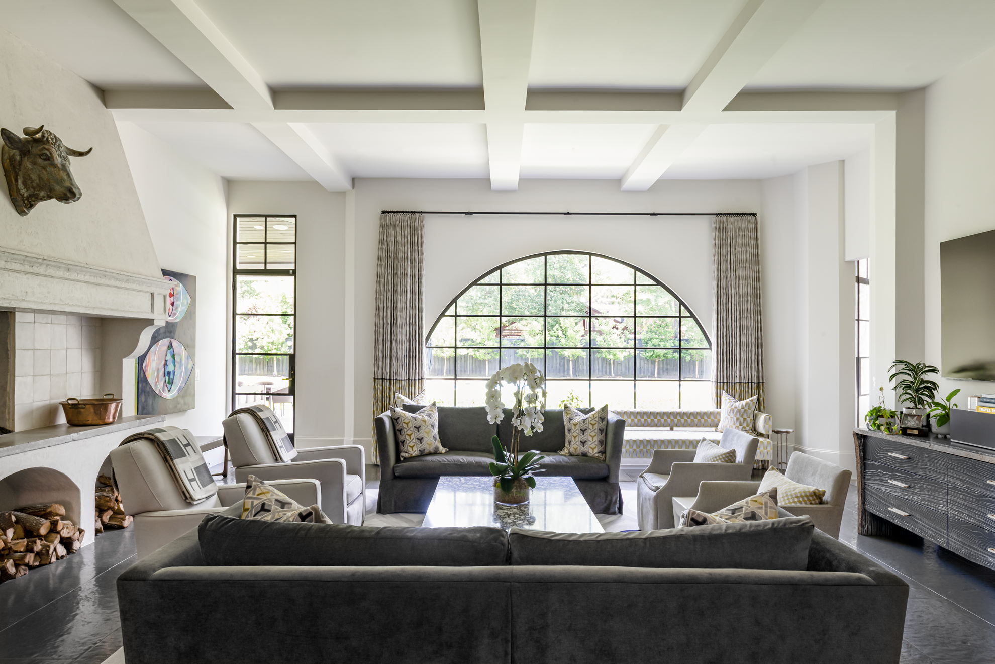 French country home in Houston family room with an arched window, charcoal seating, limestone fireplace and artwork.