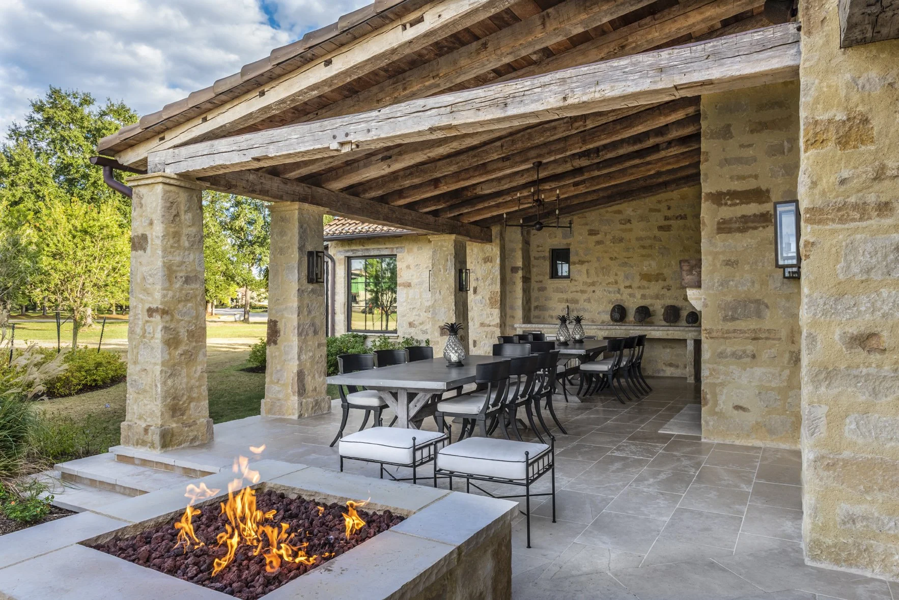 Houston Oaks ranch outdoor dining area with stone columns, reclaimed wood beams and a contemporary fire pit.