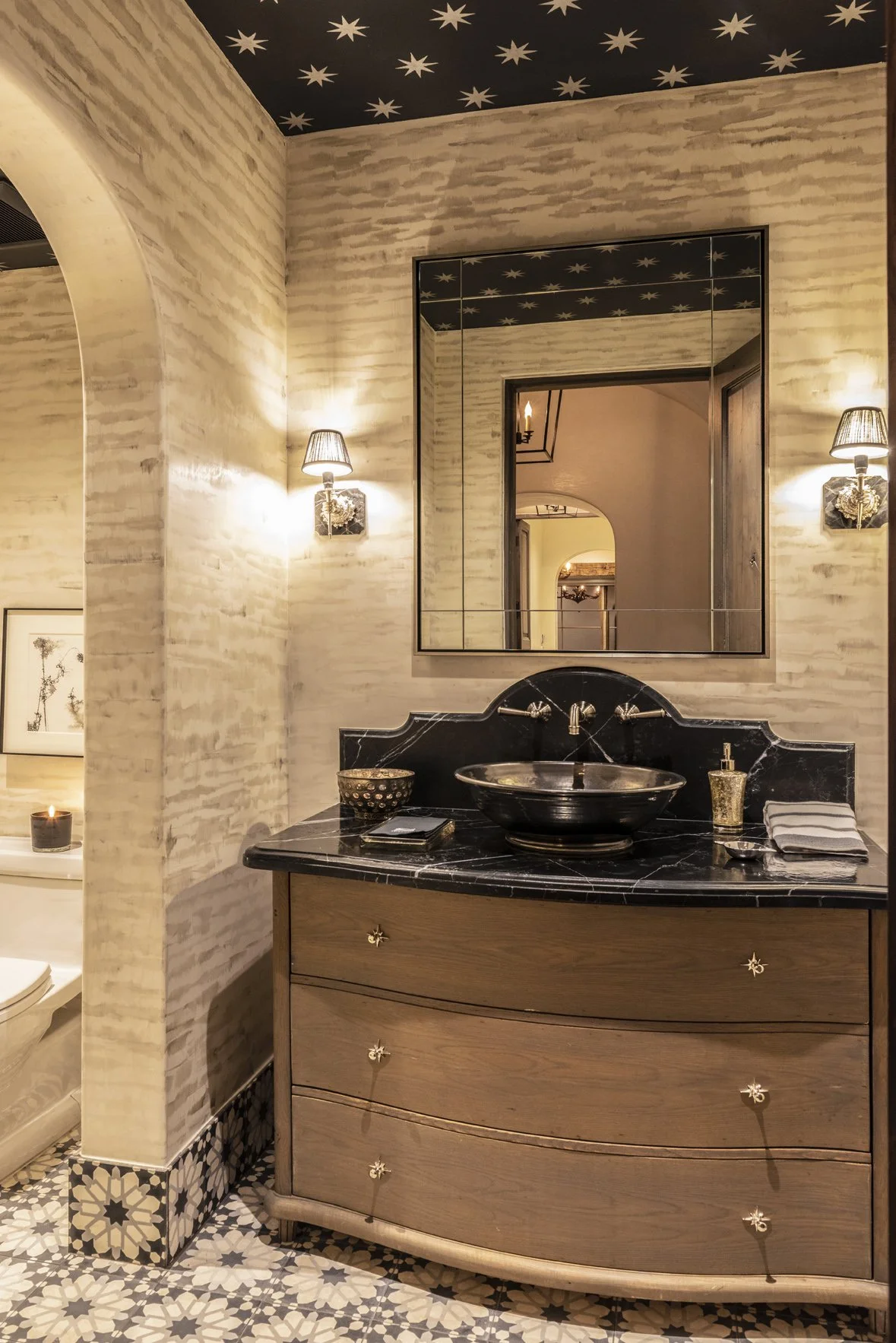 Luxury ranch powder room with a black stone basin, curved wood vanity, patterned tile floor and a dark star-patterned ceiling.