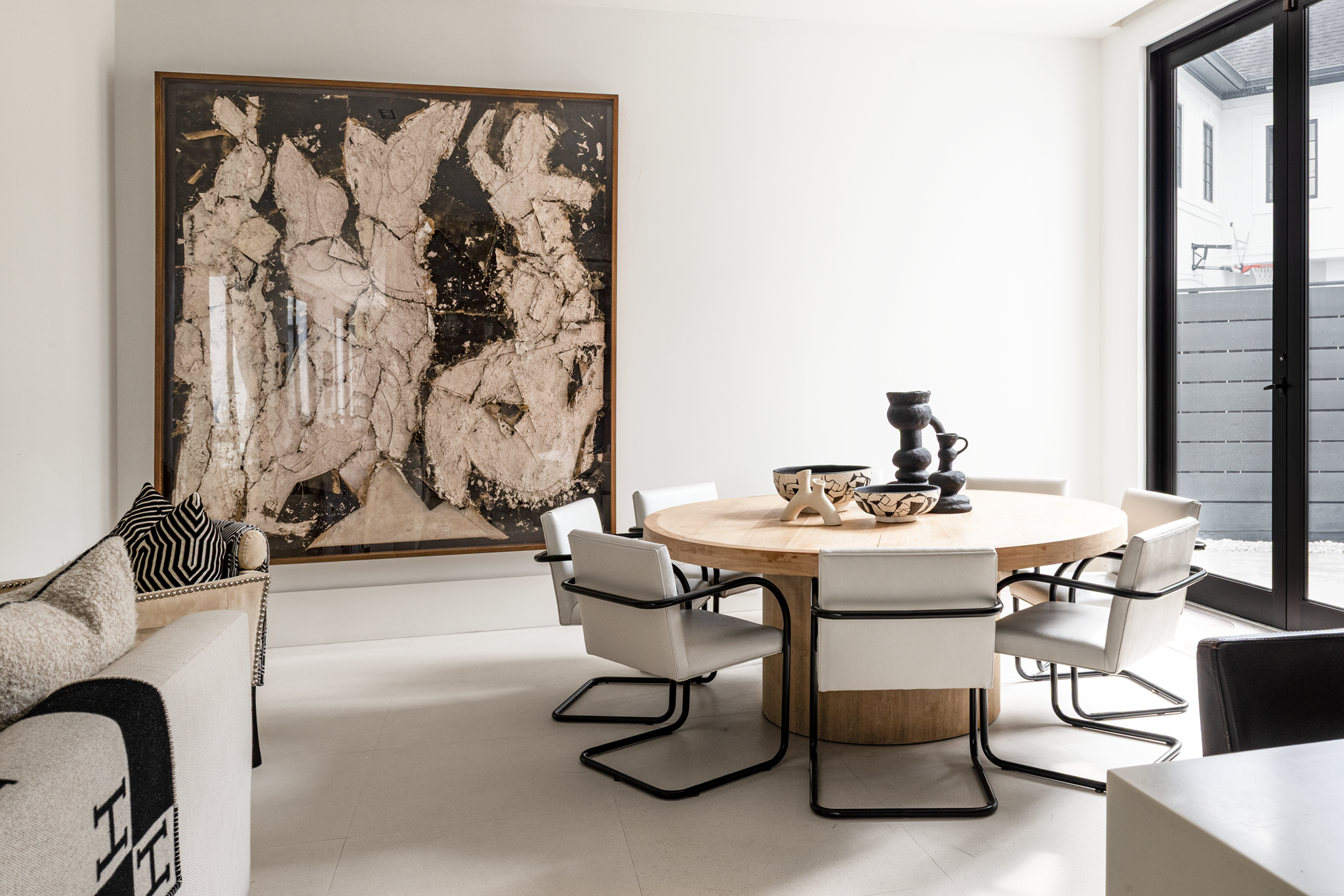 Modern luxury home in Houston breakfast room with a round wood table, white chairs and oversized abstract artwork.