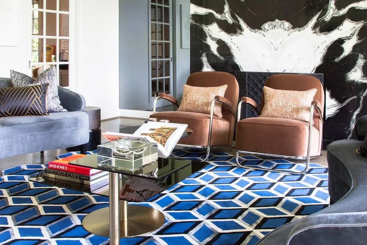 SoHo interior with a bold blue geometric rug, blush lounge chairs, black marble fireplace and contemporary art.