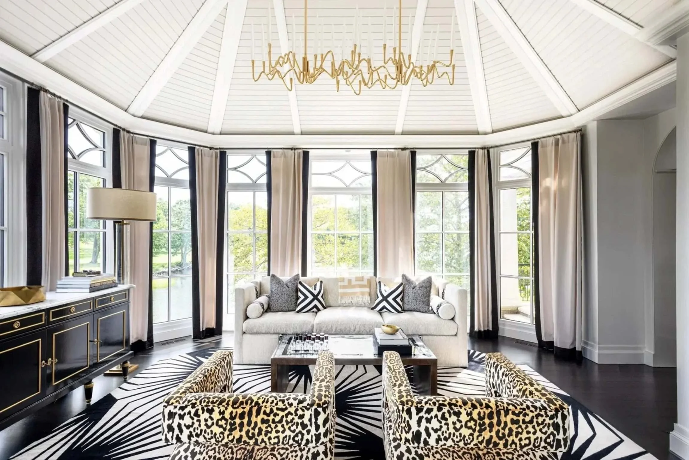 Light-filled Greenwich residence sunroom with leopard-print chairs, monochrome textiles and a sculptural brass chandelier.