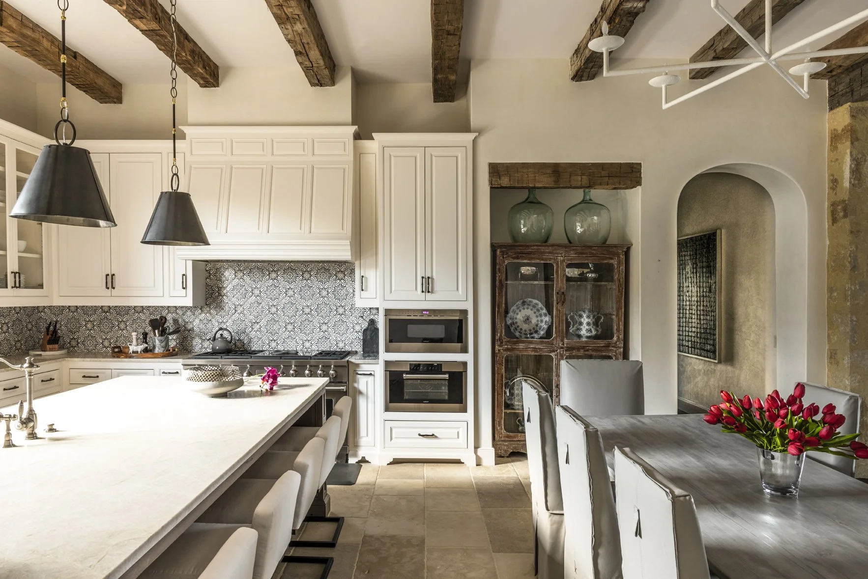 Texas ranch kitchen interior with a large island, white cabinetry, reclaimed beams, patterned tile and dining chairs.
