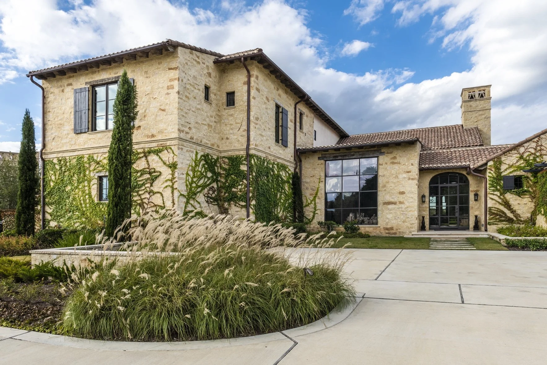 Modern Texas ranch exterior at Houston Oaks with stone walls, tiled roof, ivy and landscaped approach.