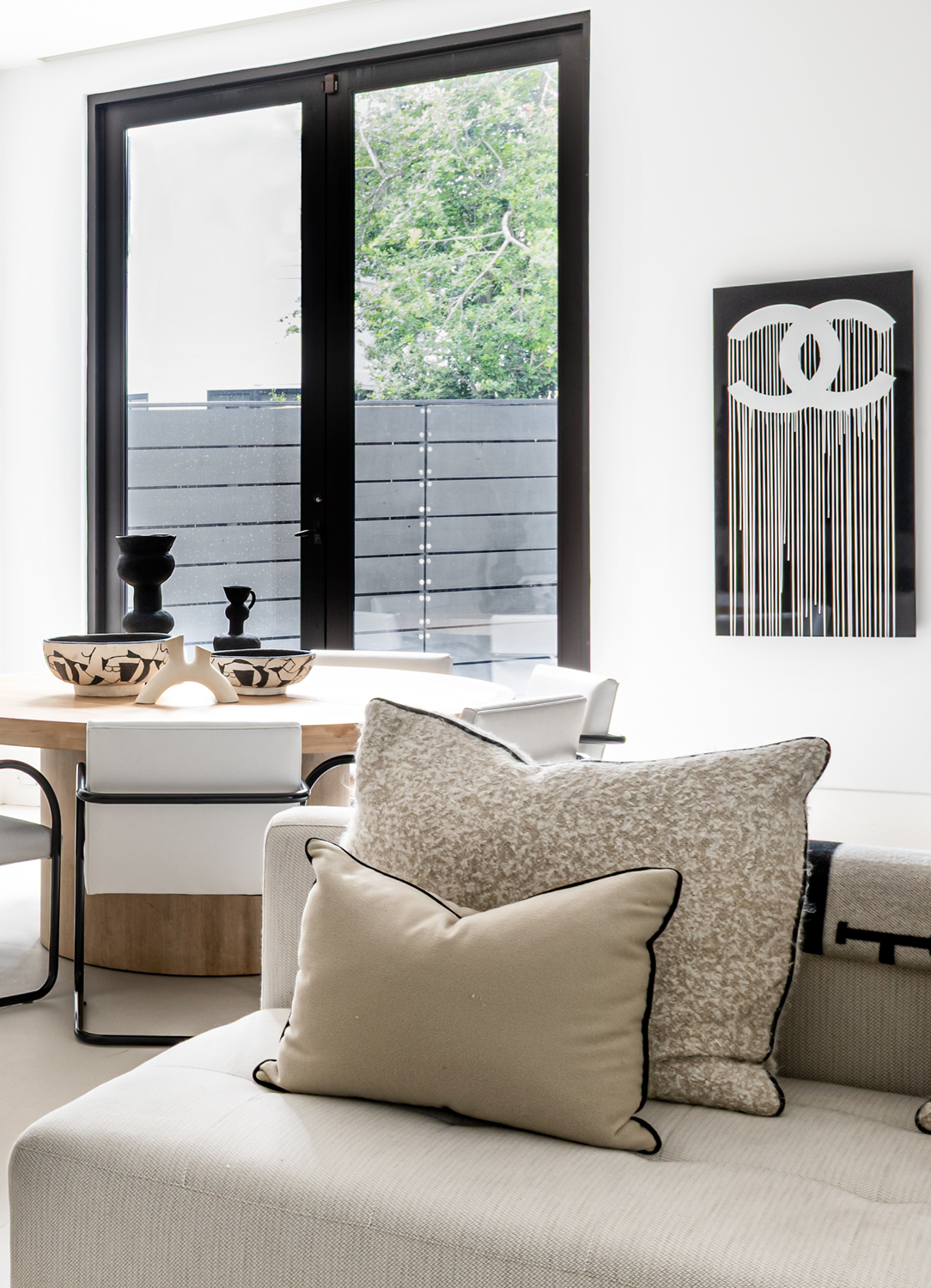 Modern luxury home in Houston dining area with a round wood table, white chairs and black-and-white Chanel artwork.