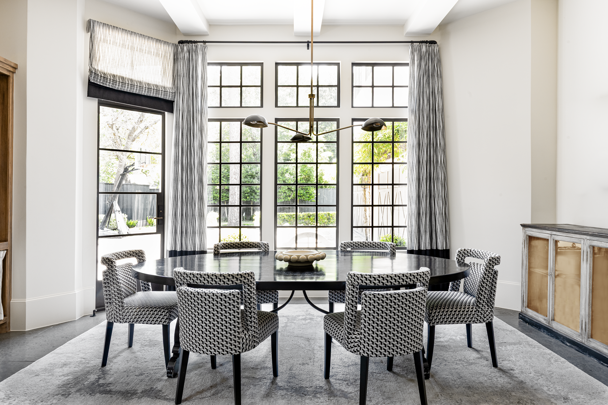 French country home in Houston breakfast room with a black round table, patterned chairs and steel-framed windows.