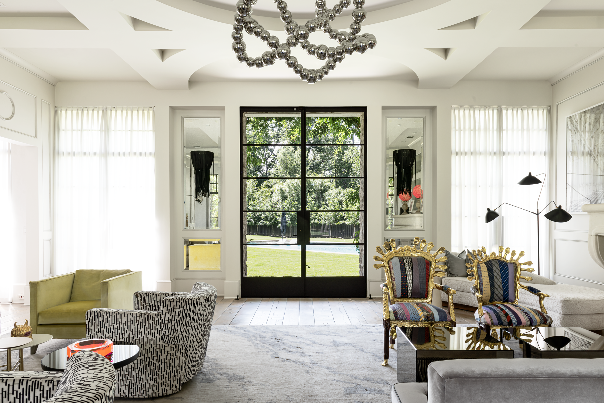 French country home in Houston living room with black-framed garden doors, statement chandelier and eclectic seating.