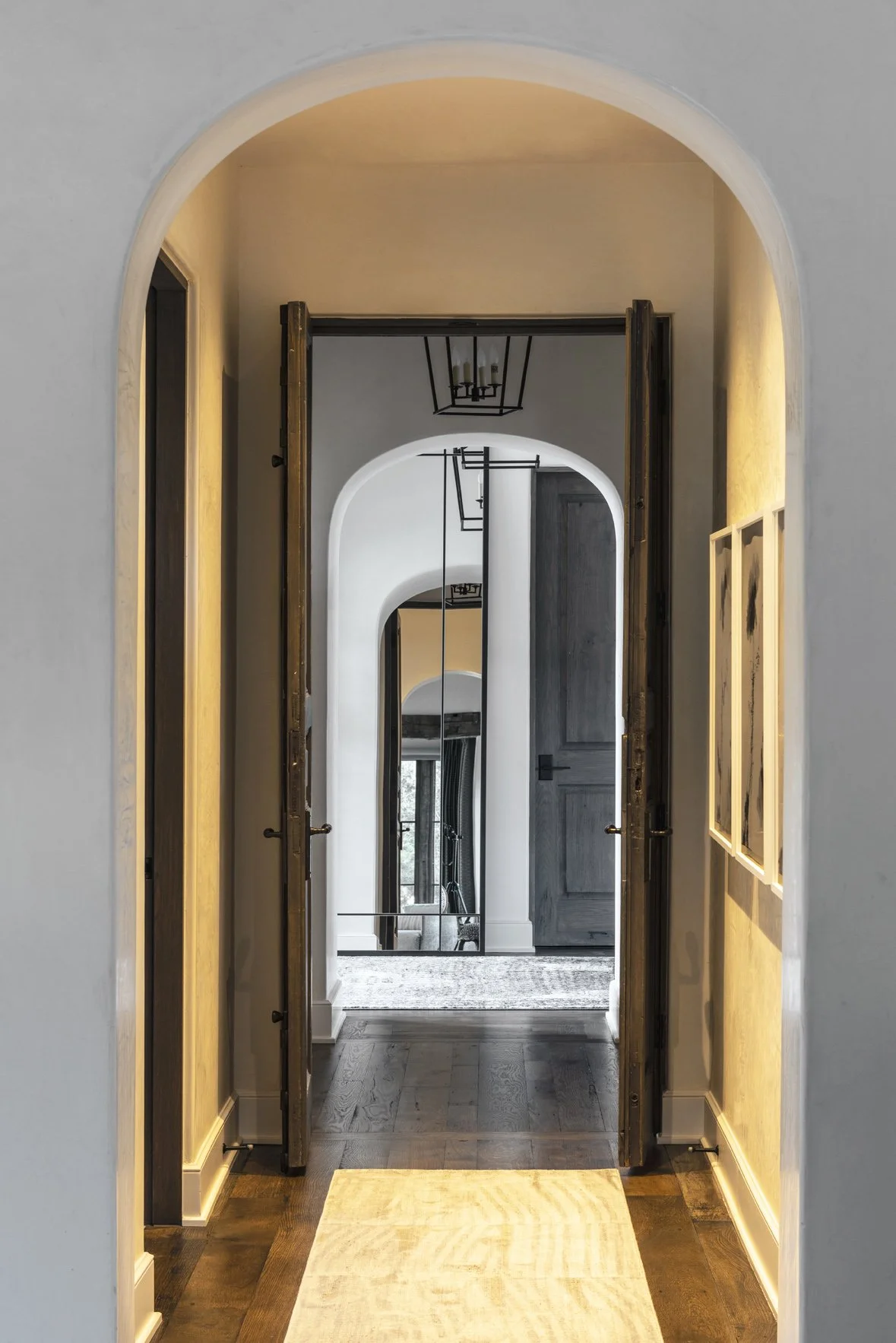 Modern ranch interior hallway with layered arches, dark wood flooring, warm wall lighting and a full-height mirror.