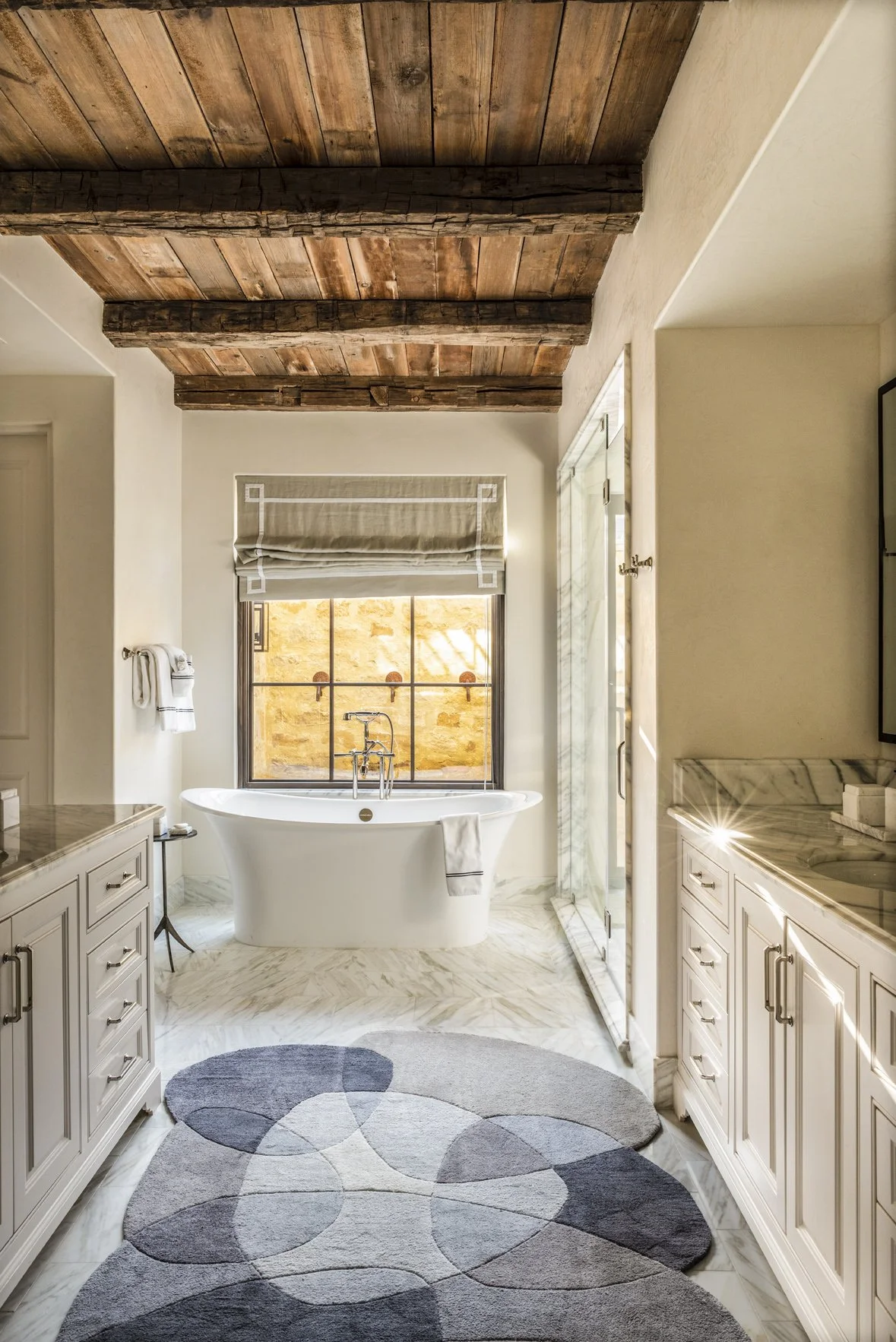 Modern ranch bathroom interior with a freestanding tub, marble flooring, white vanities and a reclaimed wood ceiling.
