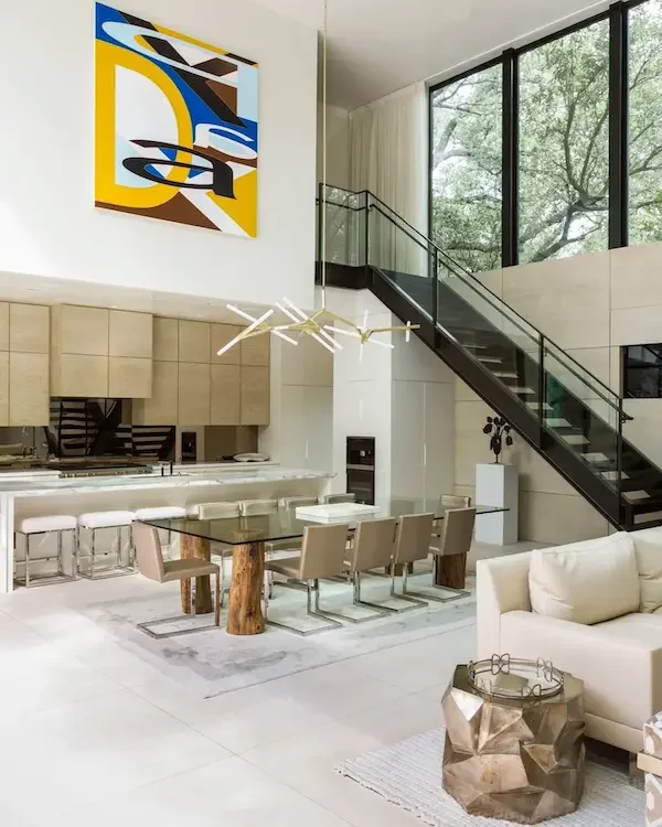 Modern double-height commercial interior design in Houston with open-plan lounge, dining area, statement art and architectural staircase