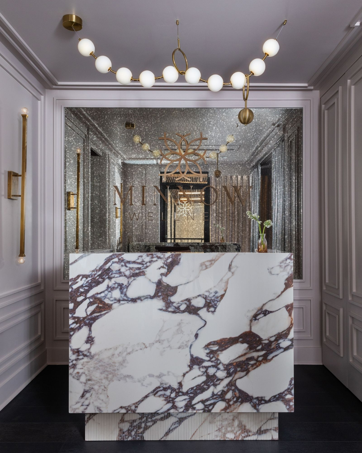 Wellness clinic Houston reception with a dramatic veined marble desk, mirrored wall and sculptural brass lighting.