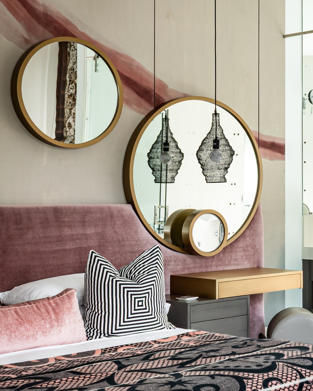 Modern luxury home in Houston primary bedroom with a pink upholstered headboard, circular mirrors and graphic bedding.