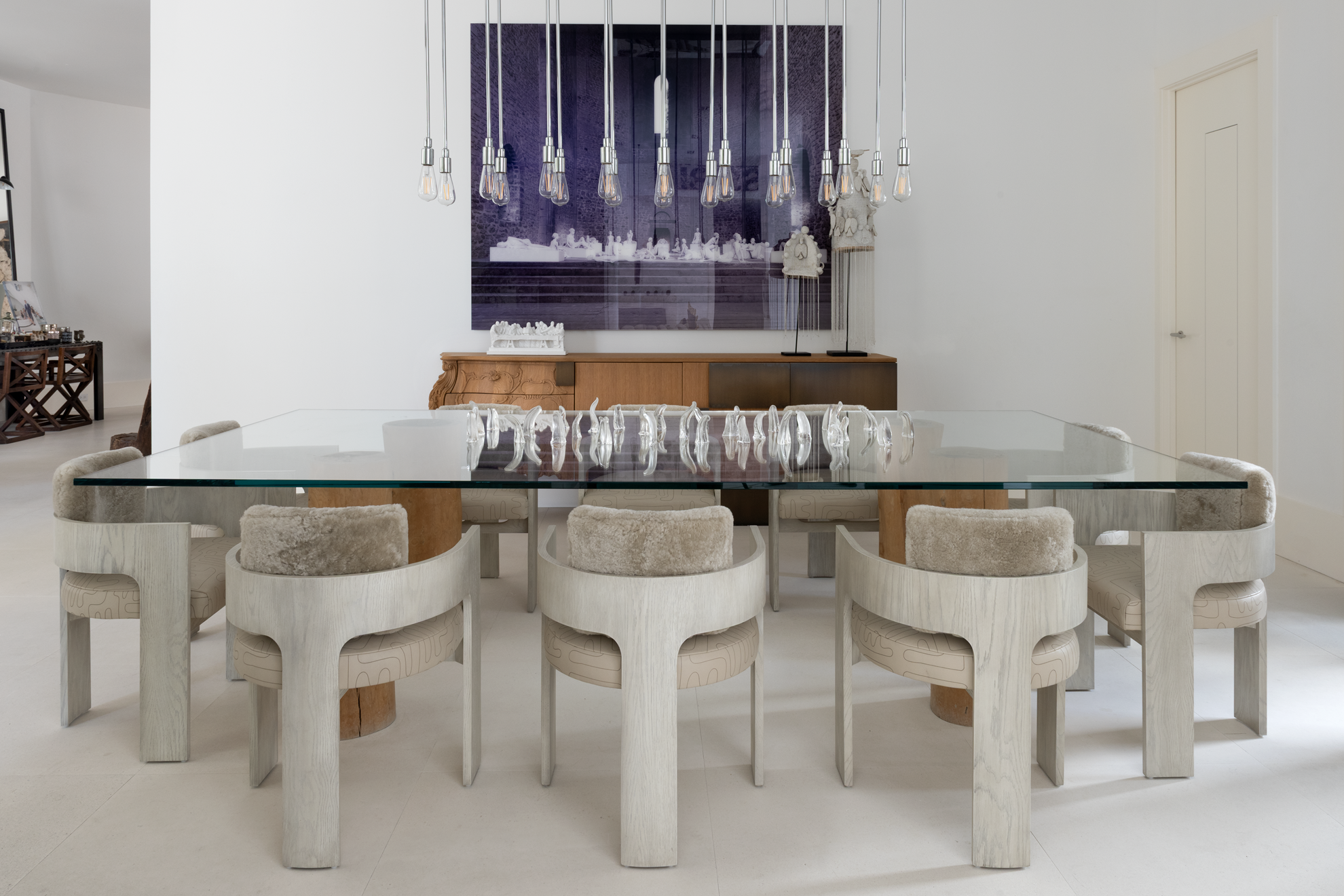 Modern luxury home in Houston dining room with a glass table, sculptural chairs, pendant bulbs and large-scale art.
