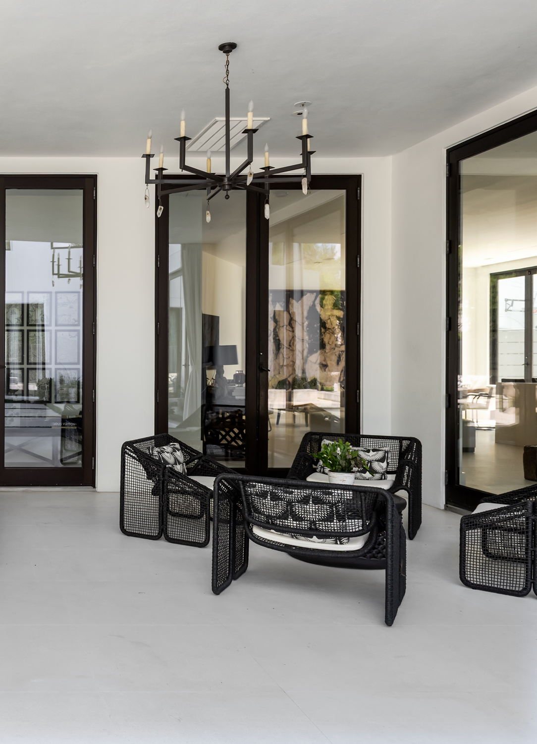 Modern luxury home in Houston covered patio with black woven lounge chairs, glazed doors and a modern chandelier.