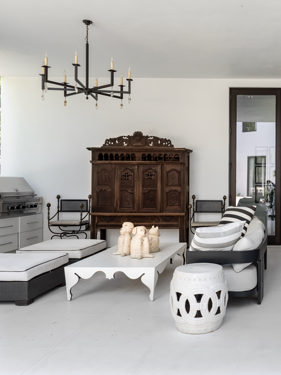 Modern luxury home in Houston covered patio with striped outdoor seating, carved wood cabinet and black chandelier.