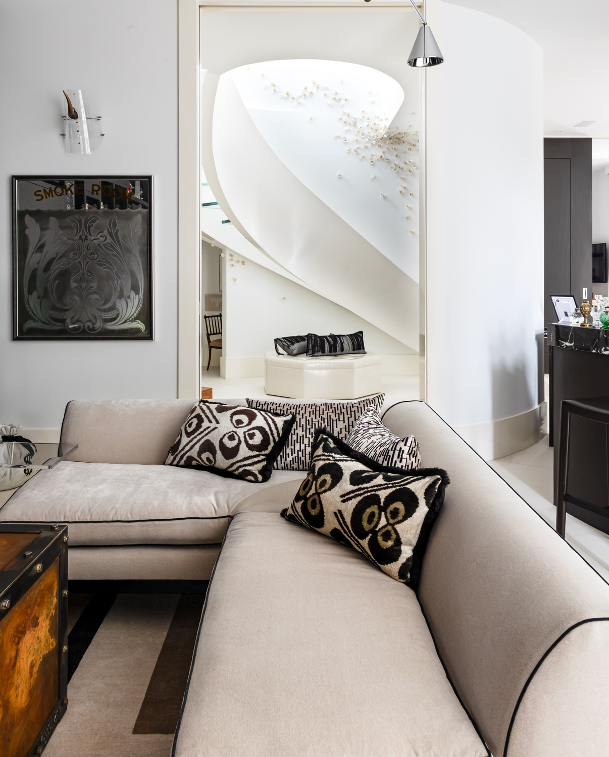Modern luxury home in Houston media room with a cream sectional, patterned pillows and a curved white staircase.