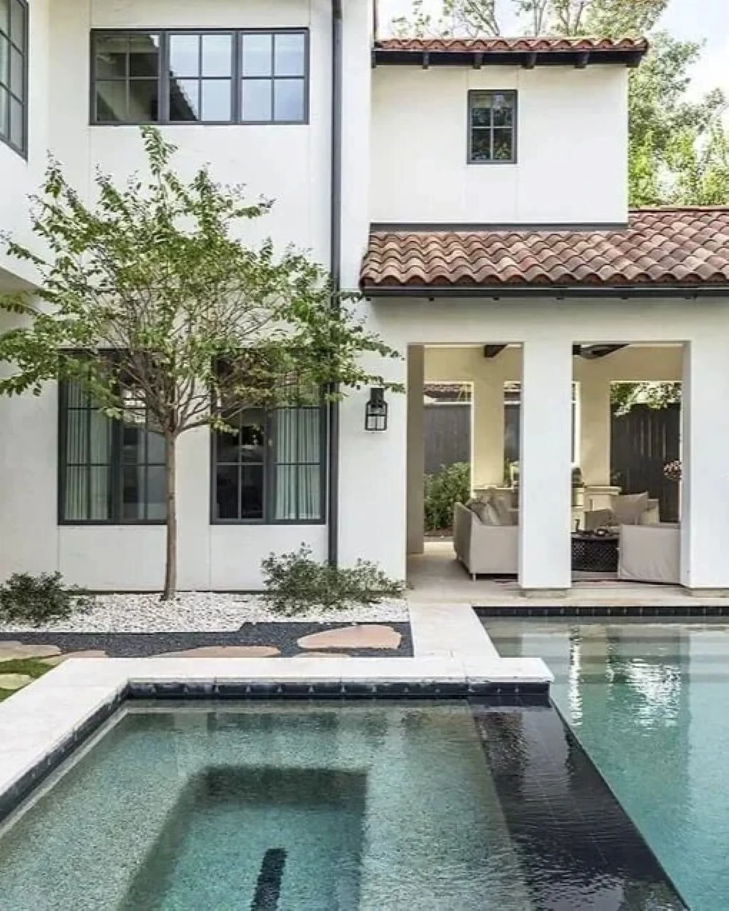 Westheimer residence pool courtyard in Houston, framed by white façades, black windows and covered outdoor seating.