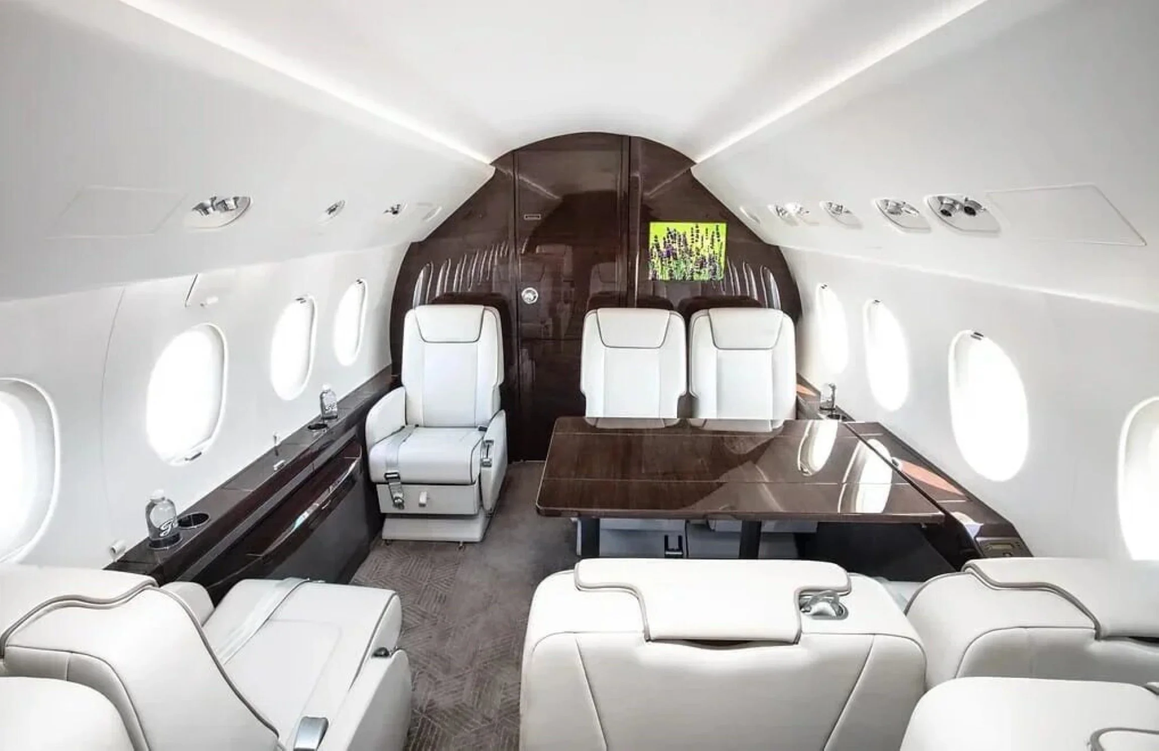 Commercial interior design project for a Falcon 2000 private jet, with white leather seating, dark wood and dining table.