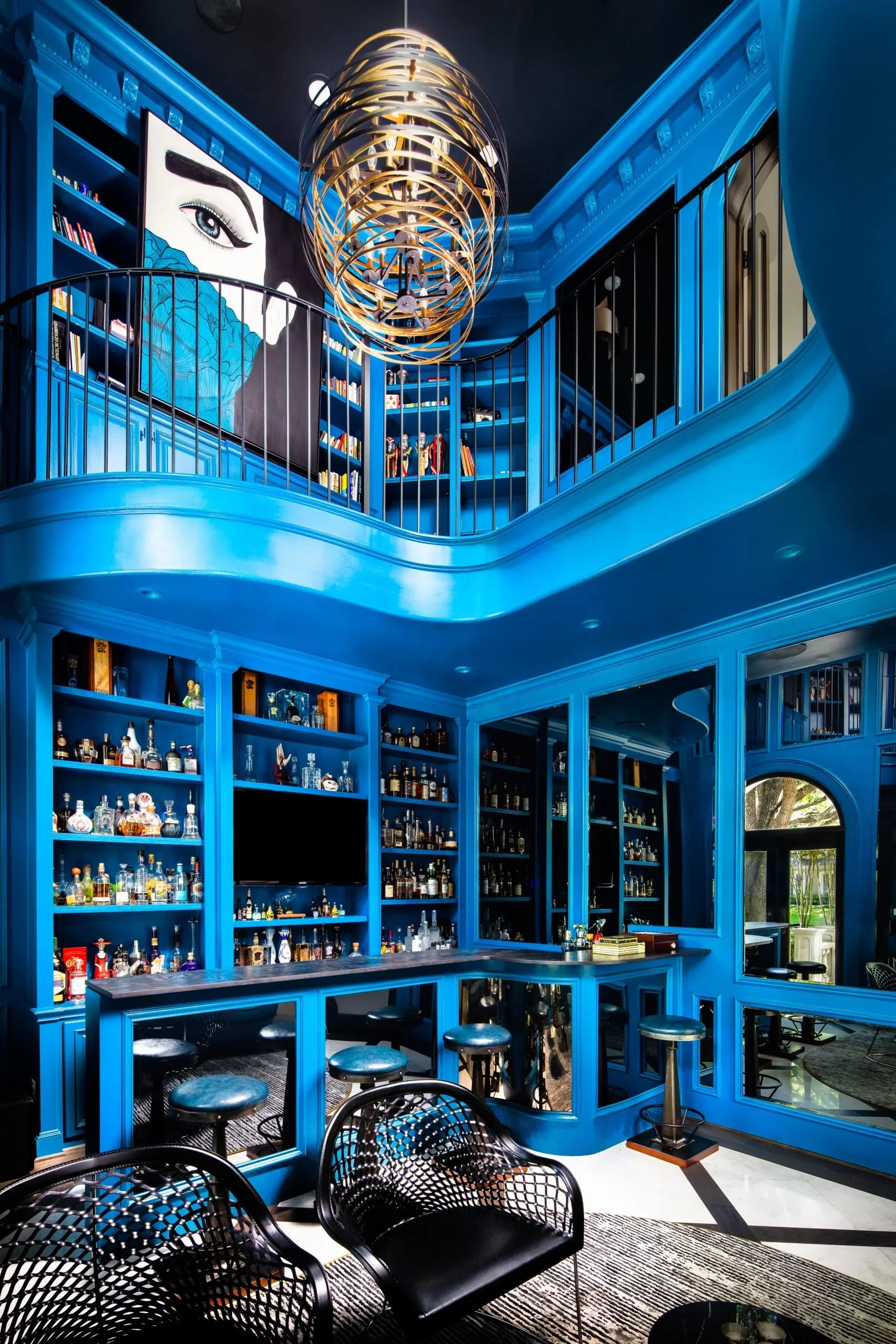 Luxury residential interior design for a custom home bar and library with bold blue cabinetry, double-height architecture, and statement lighting