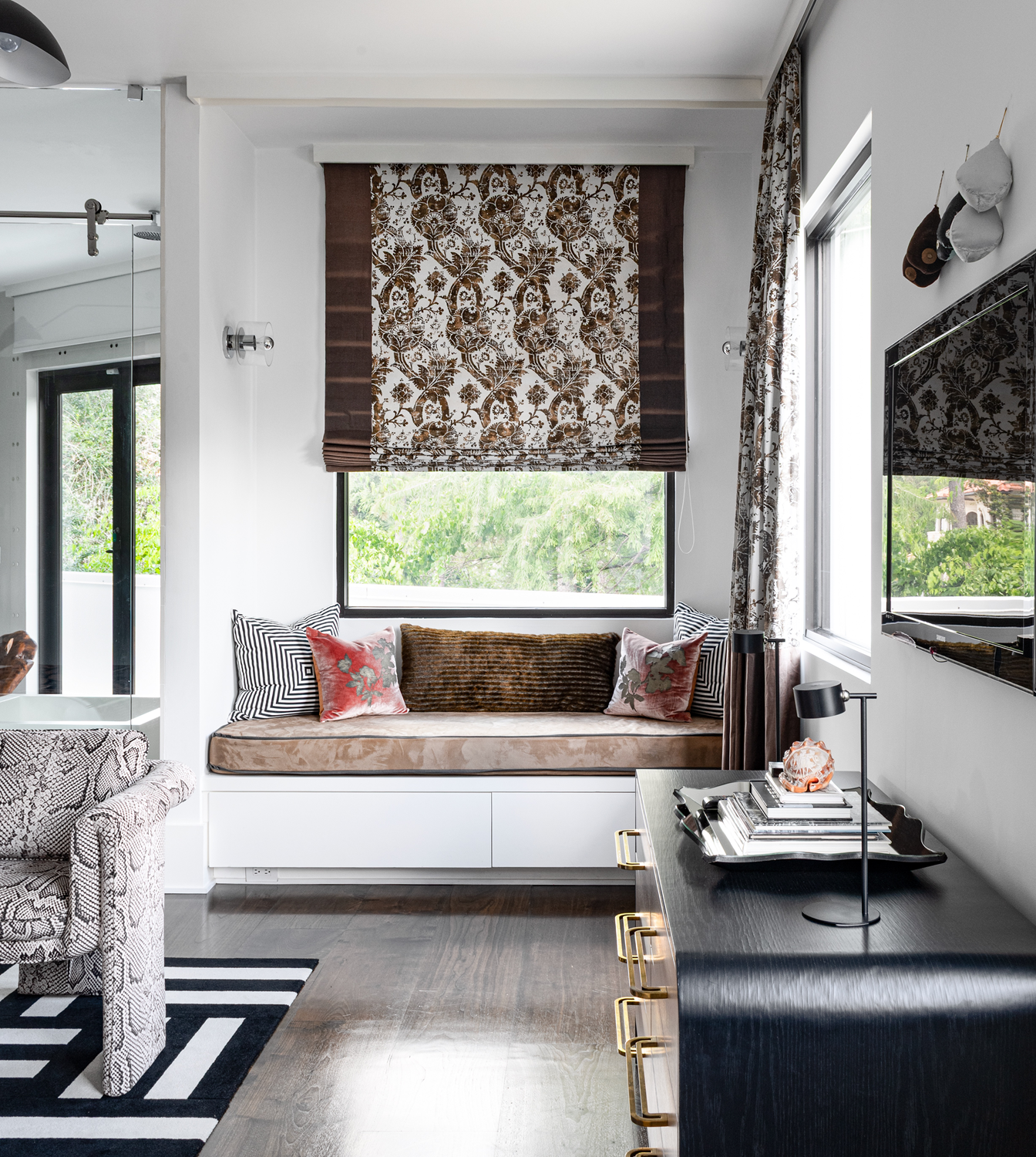 Modern luxury home in Houston guest bedroom with a built-in window seat, patterned Roman shade and black cabinetry.