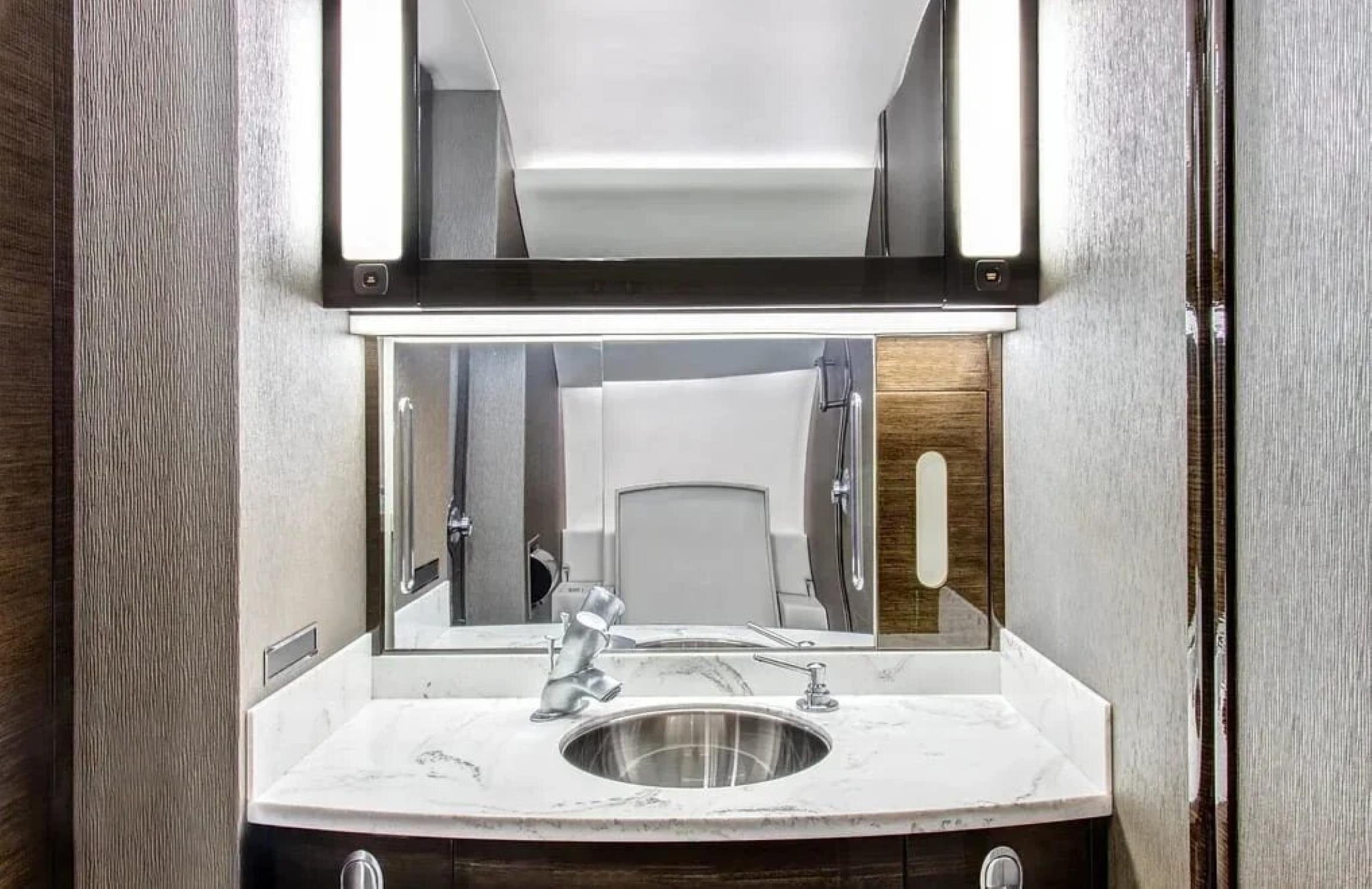 Falcon 2000 private jet lavatory with marble vanity, illuminated mirror and dark wood cabinetry.