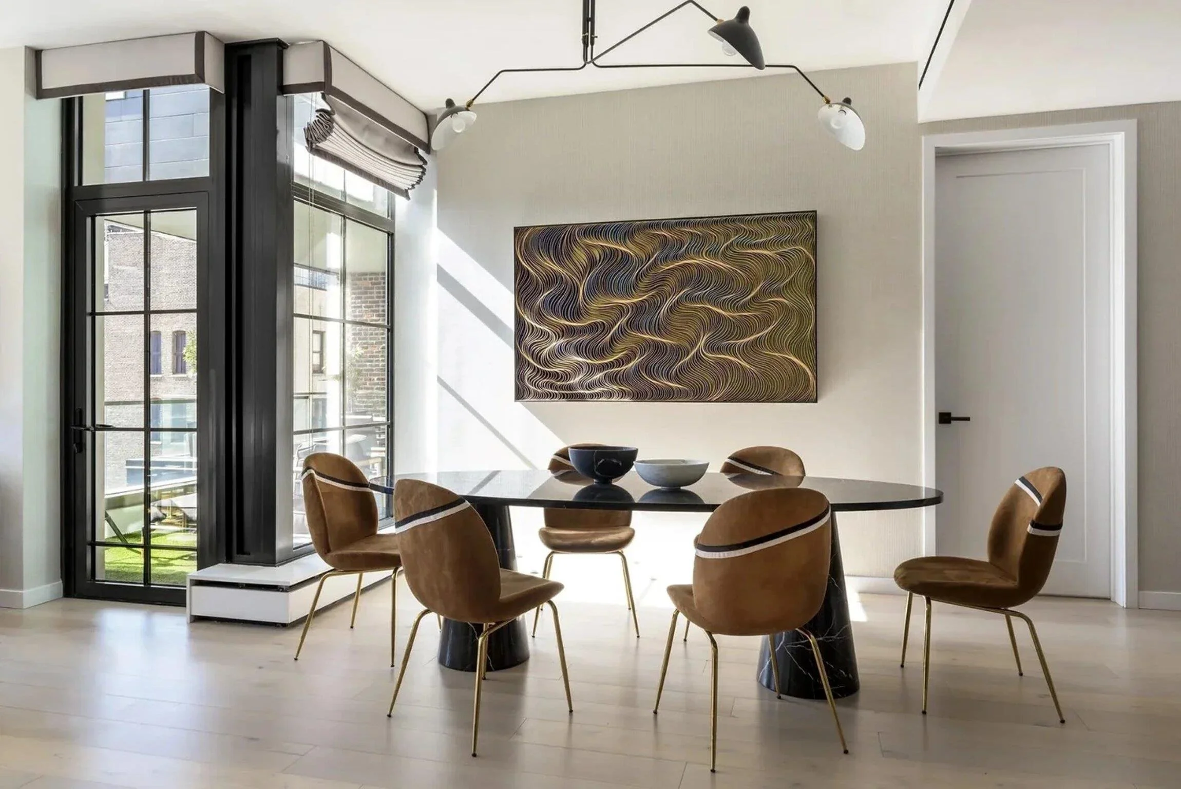 Chelsea pied-à-terre dining room with sculptural lighting, curved brown chairs, a black table and contemporary artwork.