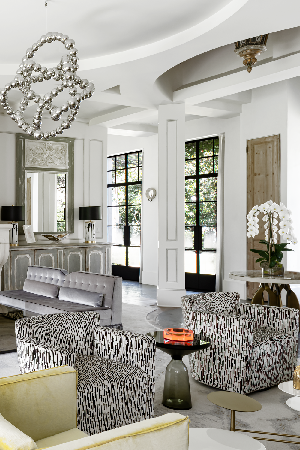 French country home in Houston sitting area with patterned armchairs, yellow velvet seating and sculptural pendant lighting.