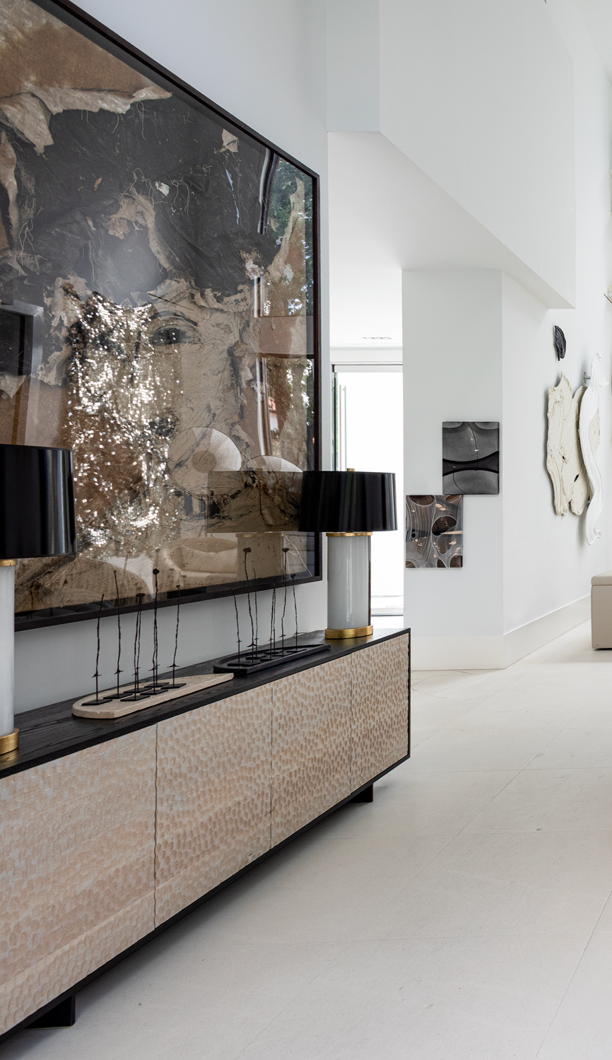 Modern luxury home in Houston entry with a textured console, black table lamps, large abstract artwork and wall sculpture.
