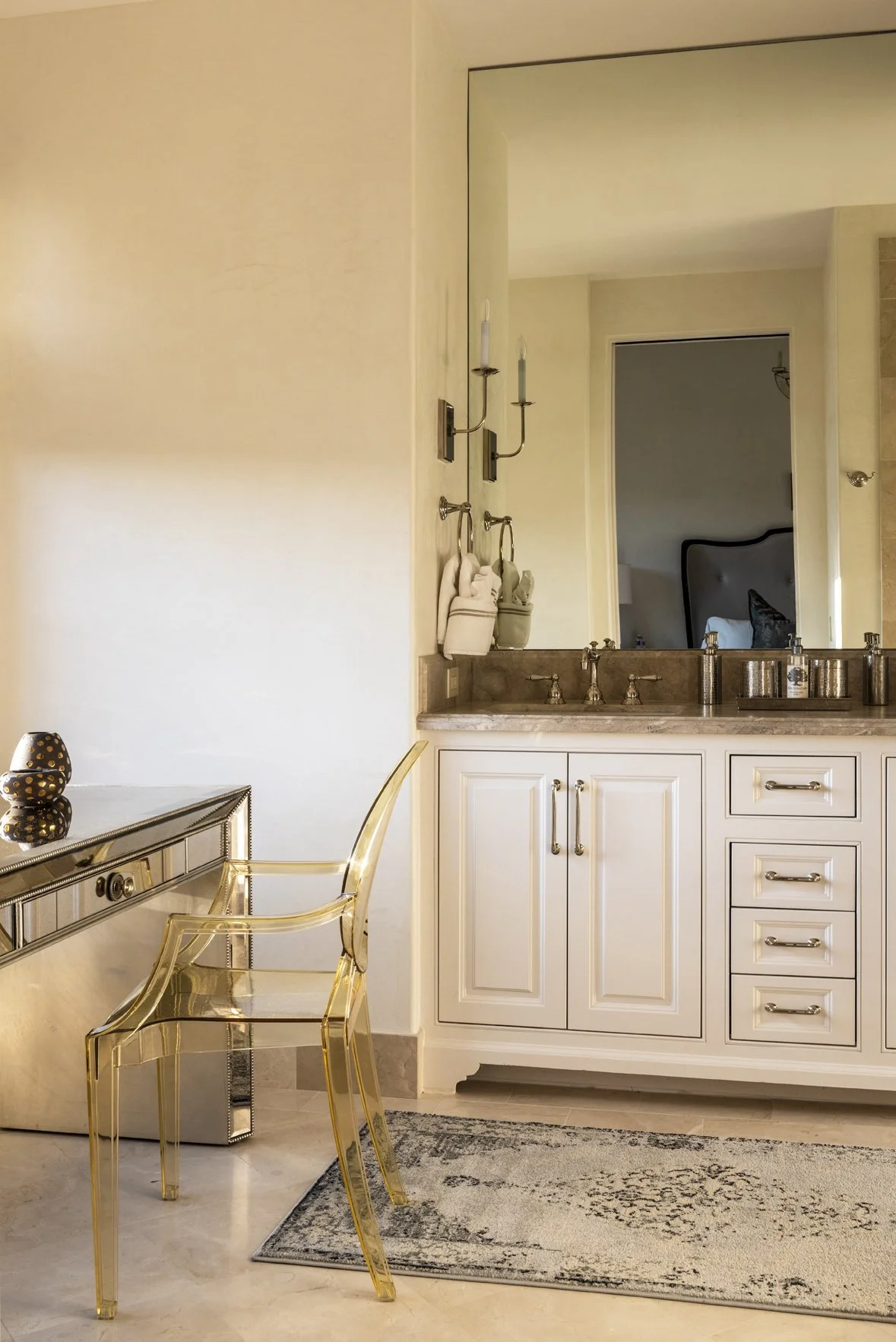 Luxury ranch bathroom dressing area with white cabinetry, a full-height mirror, clear acrylic chair and mirrored console.