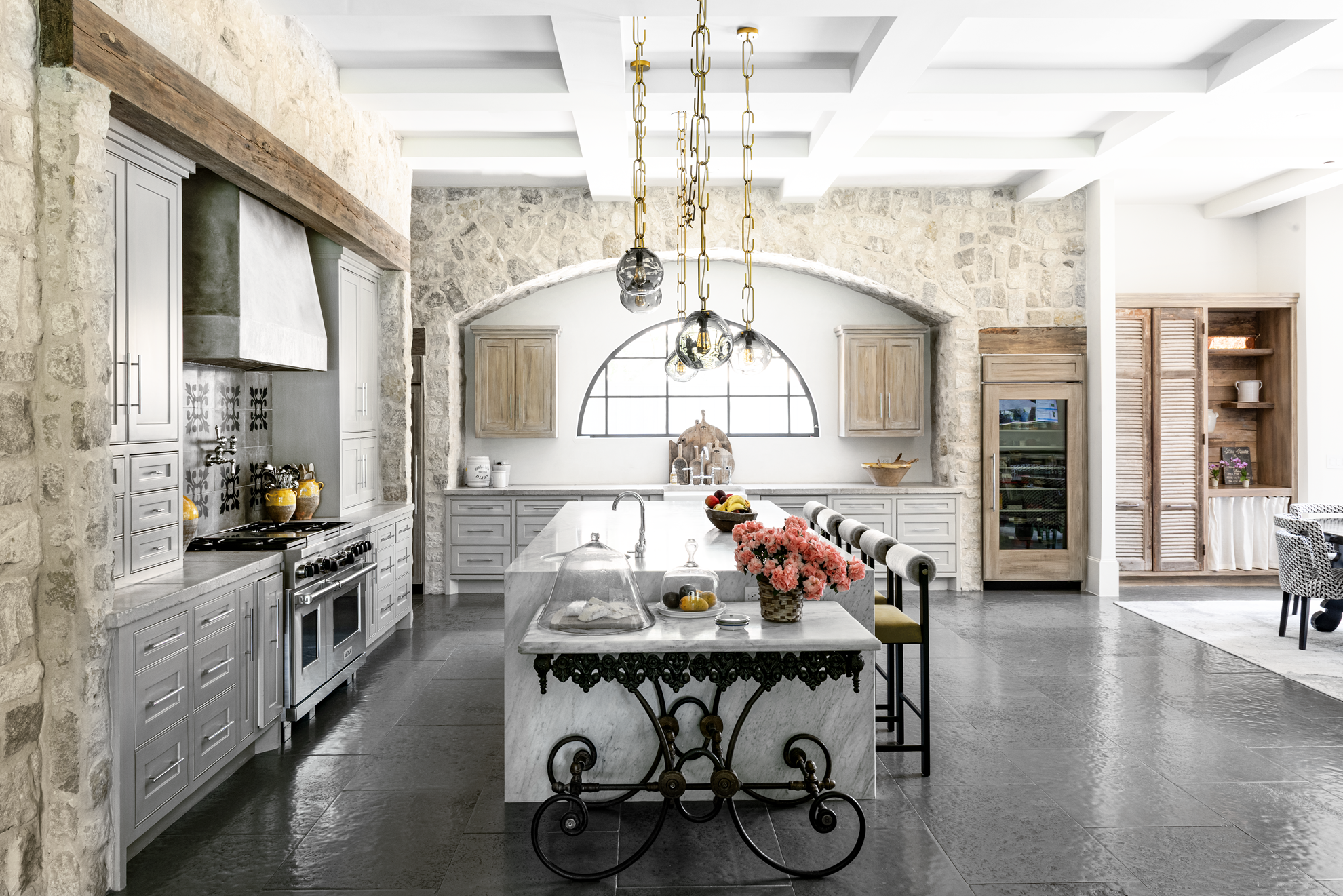 French country home in Houston kitchen with limestone walls, pale cabinetry, marble islands and glass pendant lights.