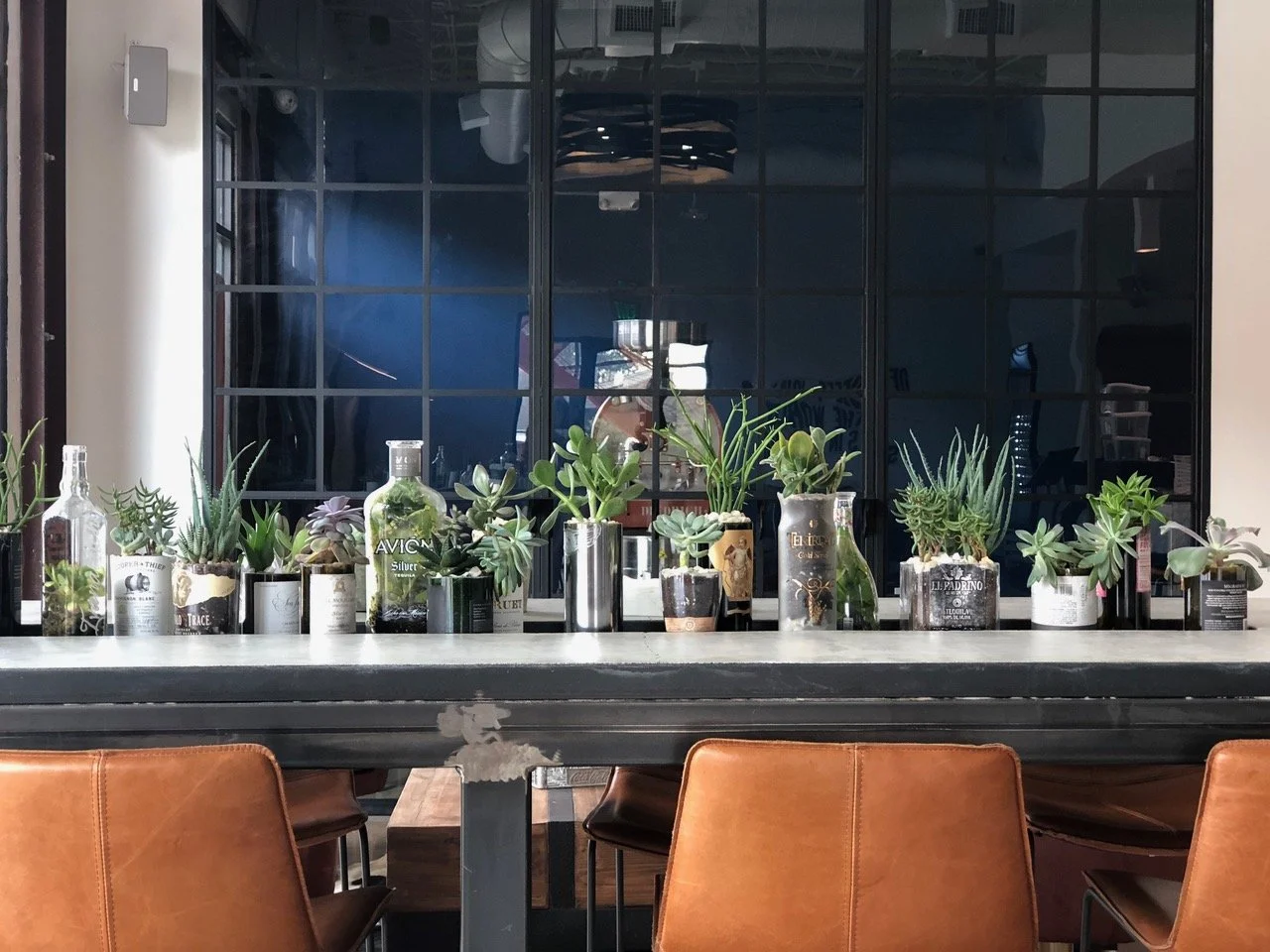 Bar and seating detail from a cafe in The Heights, Houston, featuring leather stools, planting, and refined hospitality interior design elements.