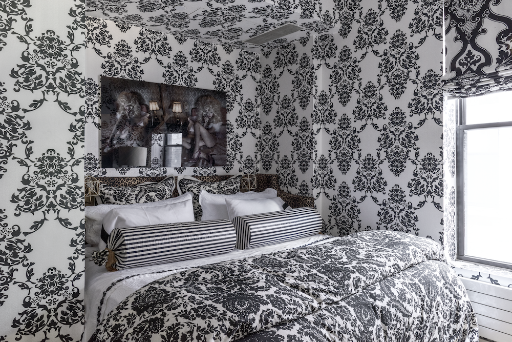 Interior designer New York bedroom with black-and-white damask wallcovering, layered bedding and a leopard headboard.