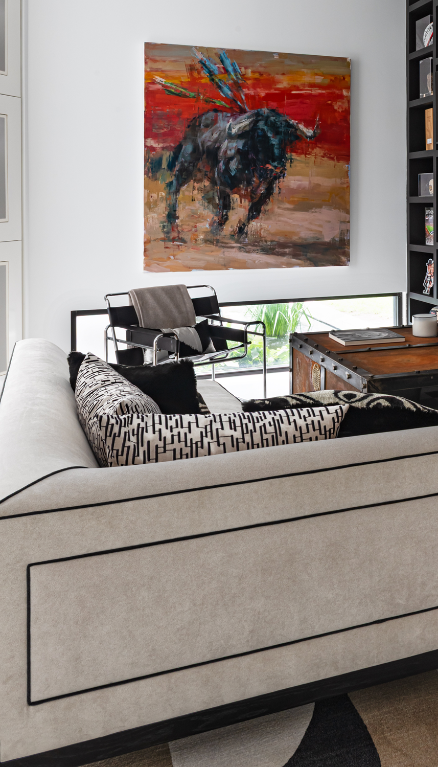 Modern luxury home in Houston TV room with a cream sofa, leather lounge chair, trunk table and colourful bull artwork.