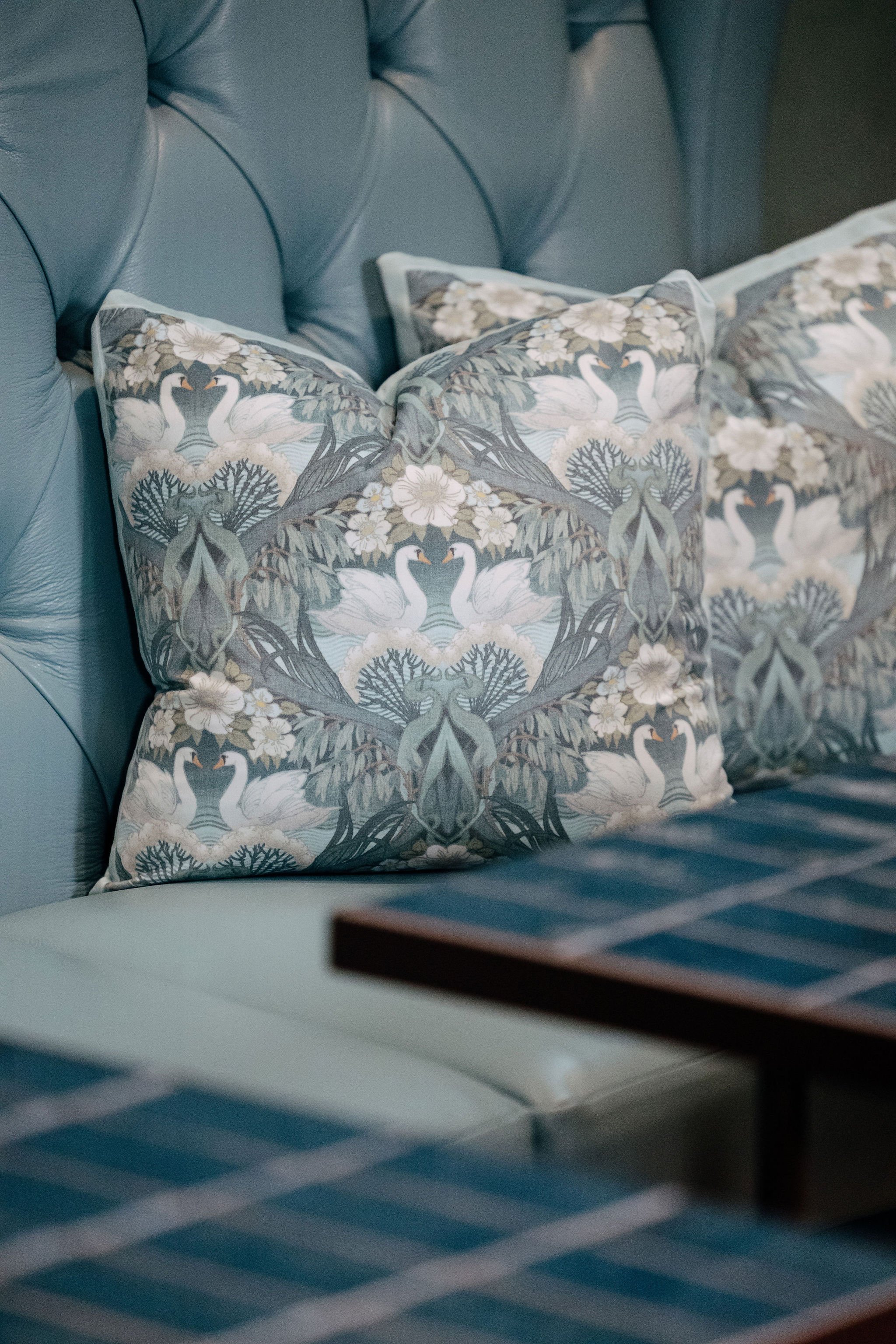 Decorative pillows with swan and floral patterns on a blue tufted leather sofa.