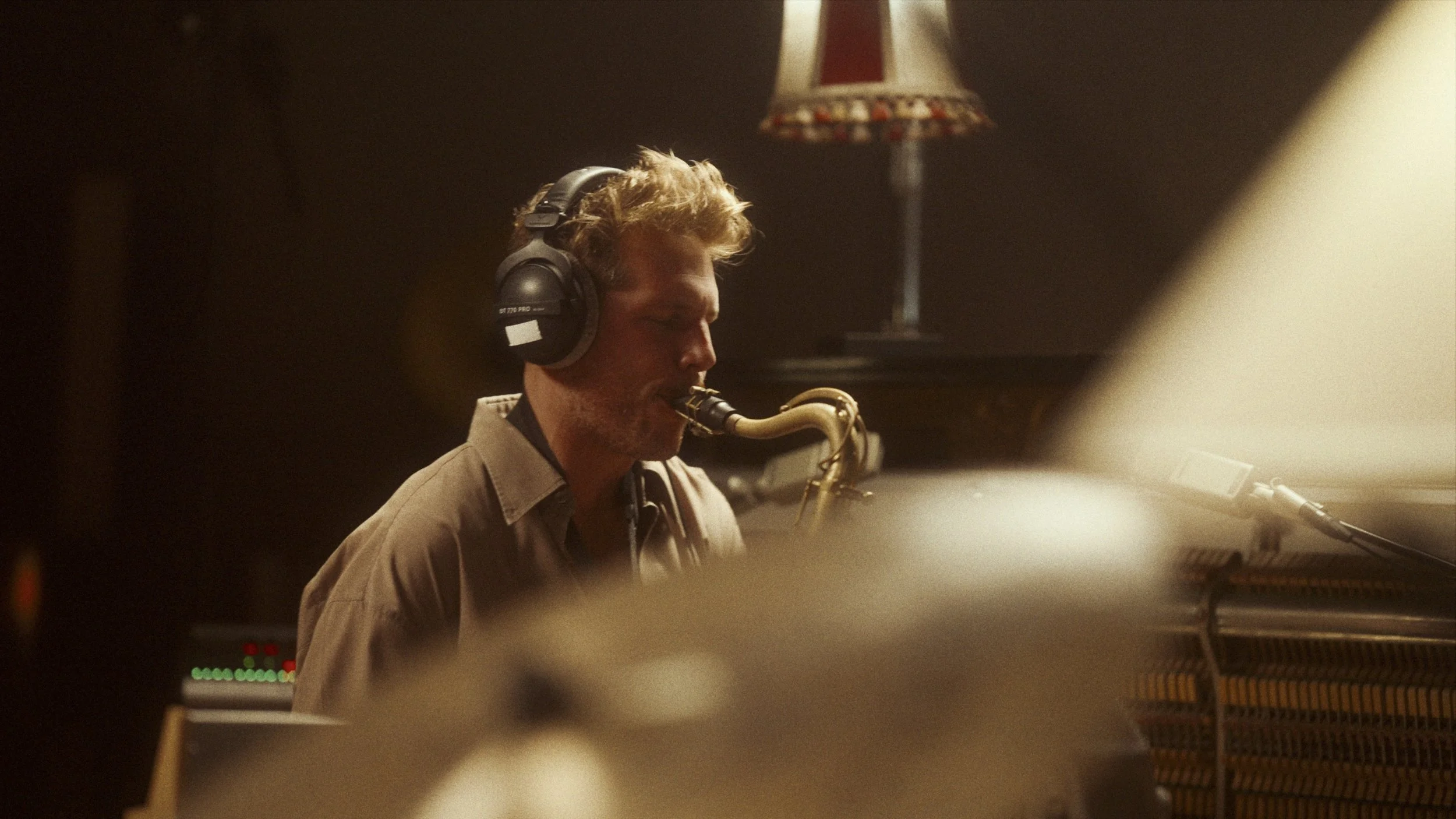 A man wearing headphones playing a saxophone in a recording studio.