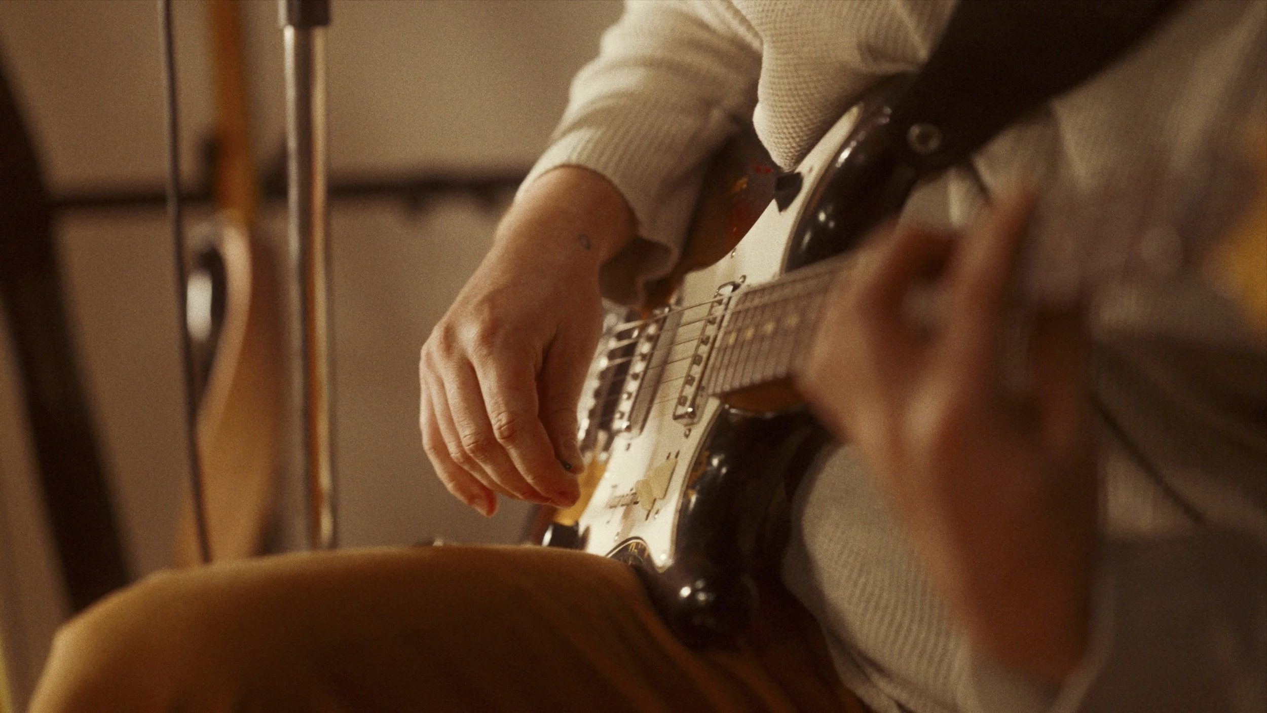 Close-up of a person playing an electric guitar, focusing on their hands on the fretboard and body of the guitar, in a warm indoor setting.
