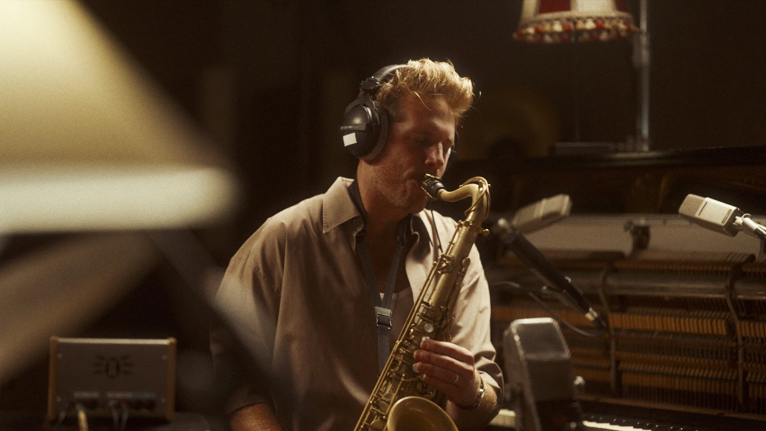 A man wearing headphones is playing a saxophone in a recording studio.