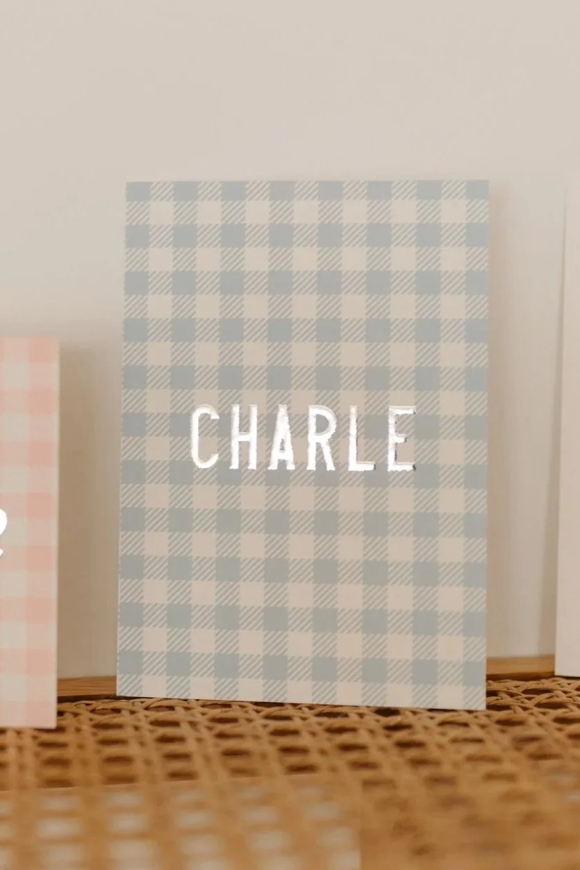 Geboortekaartje met blauwe en gebroken wit geruite achtergrond en de naam 'CHARLE' in witte letters