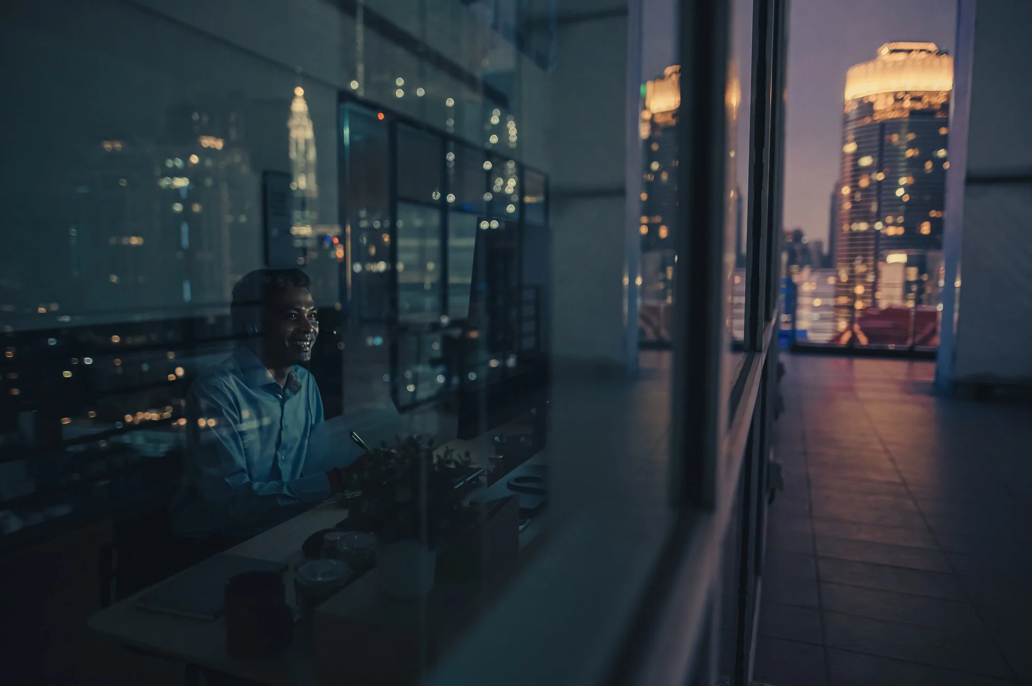 Cityscape with modern glass and concrete buildings at sunset, featuring winding roads with light trails from moving vehicles.