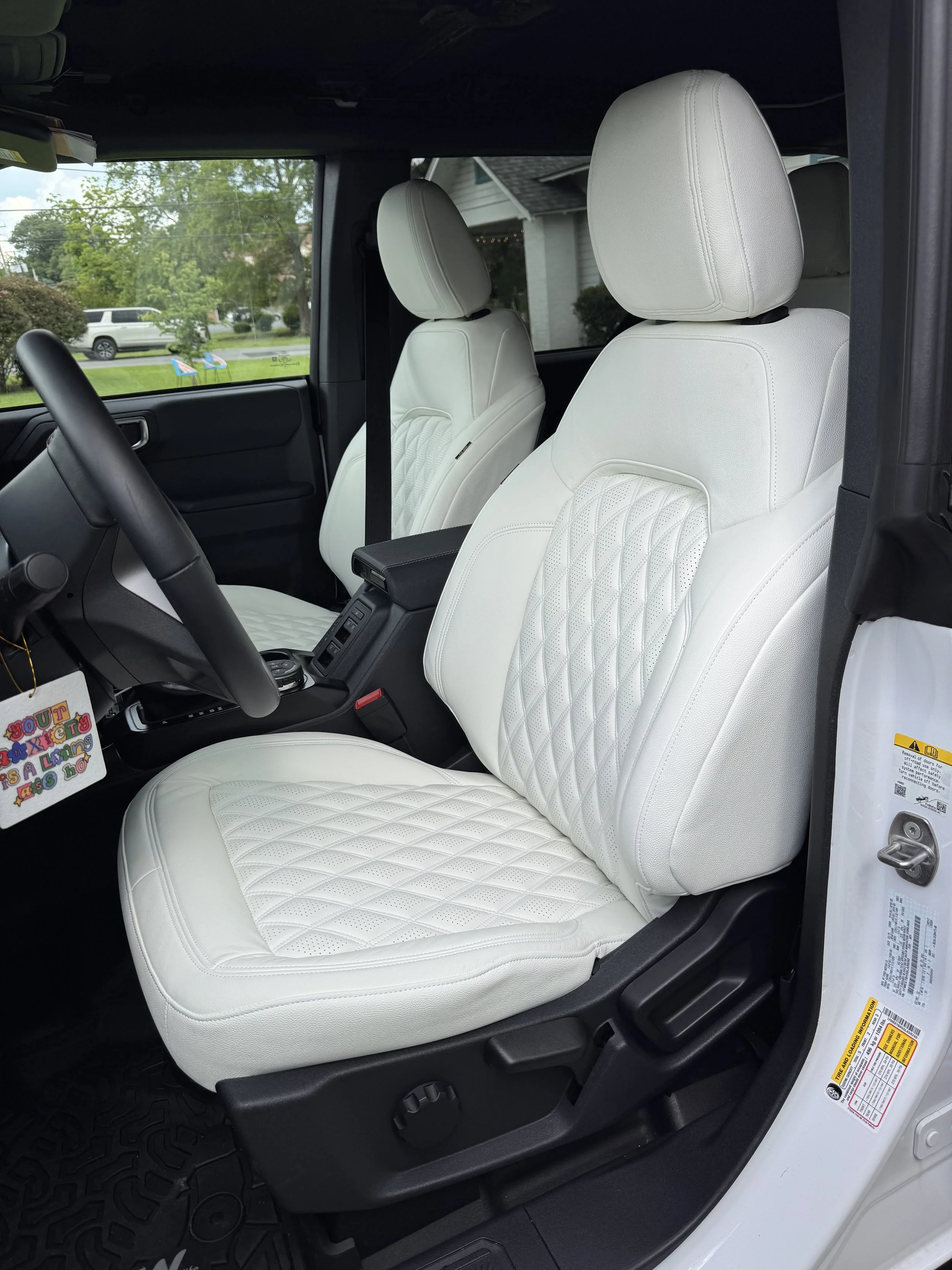 Interior of a vehicle showcasing white, diamond-stitched leather seats with black accents and a view of the outside through the window.