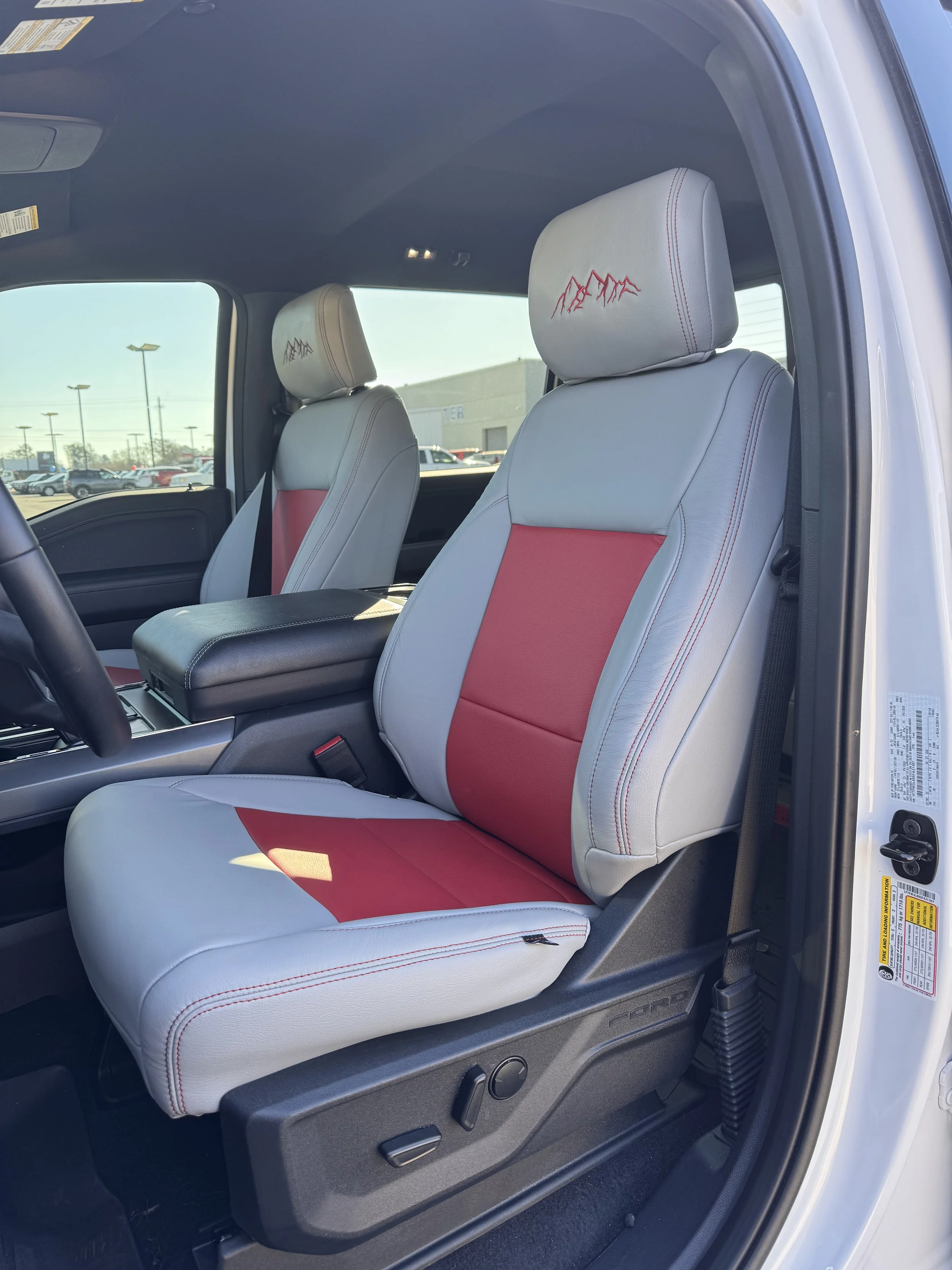 Front seats of a vehicle with white and red seat covers, featuring a mountain design embroidered on the headrests.
