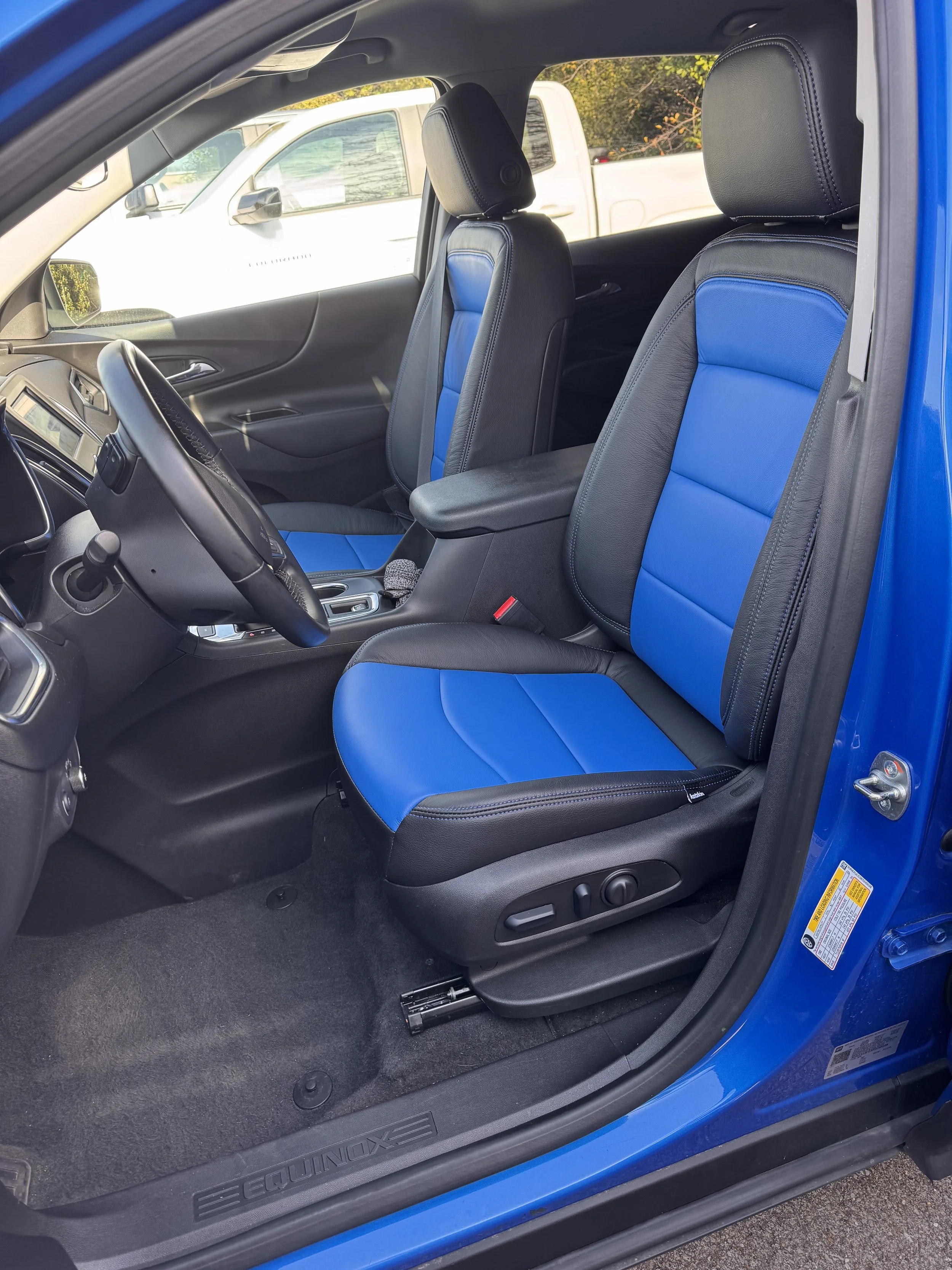 The interior of a blue vehicle showing the front seats with black and blue upholstery, the dashboard, steering wheel, and driver side door.