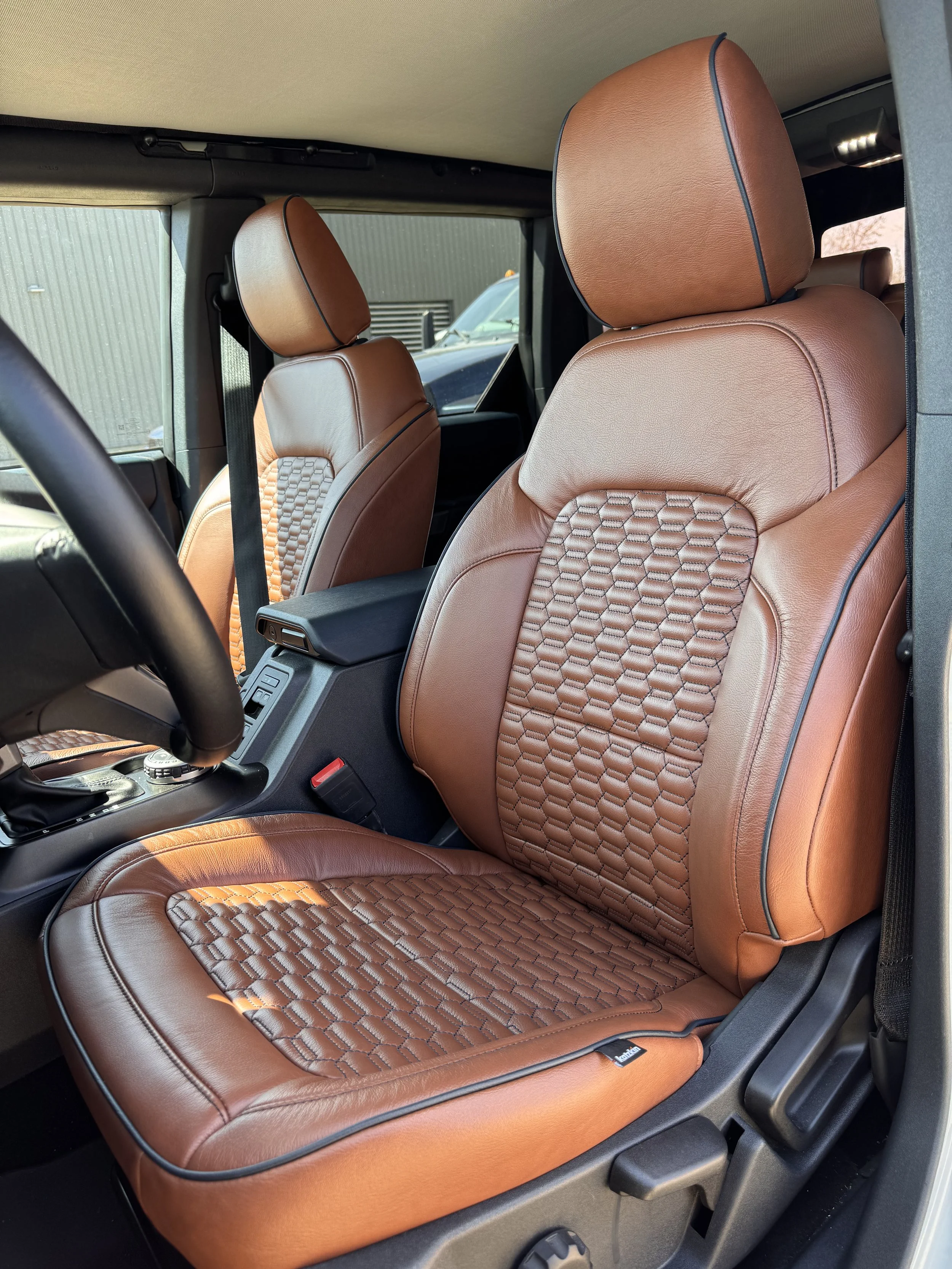 Front passenger and driver seats inside a vehicle with brown leather upholstery that has a textured pattern in the center.