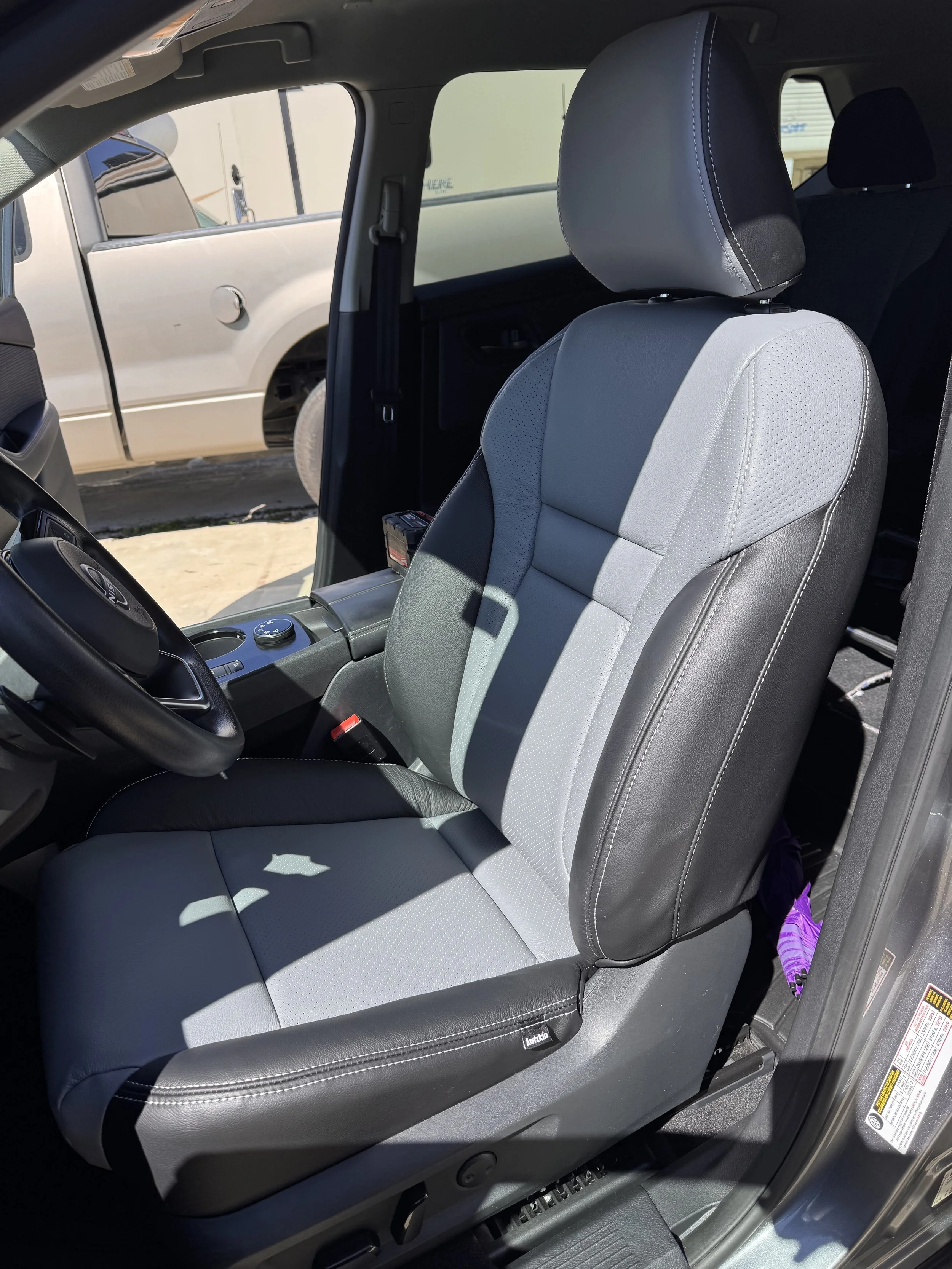 Front passenger seat of a truck with two-tone gray seat upholstery and black leather sides, with a headrest and shadowed area on the seat.