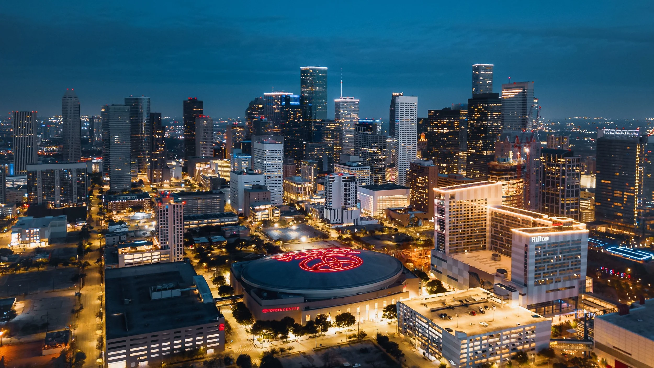 Downtown Houston, Texas skyline at dusk, featuring illuminated office towers and the Toyota Center.