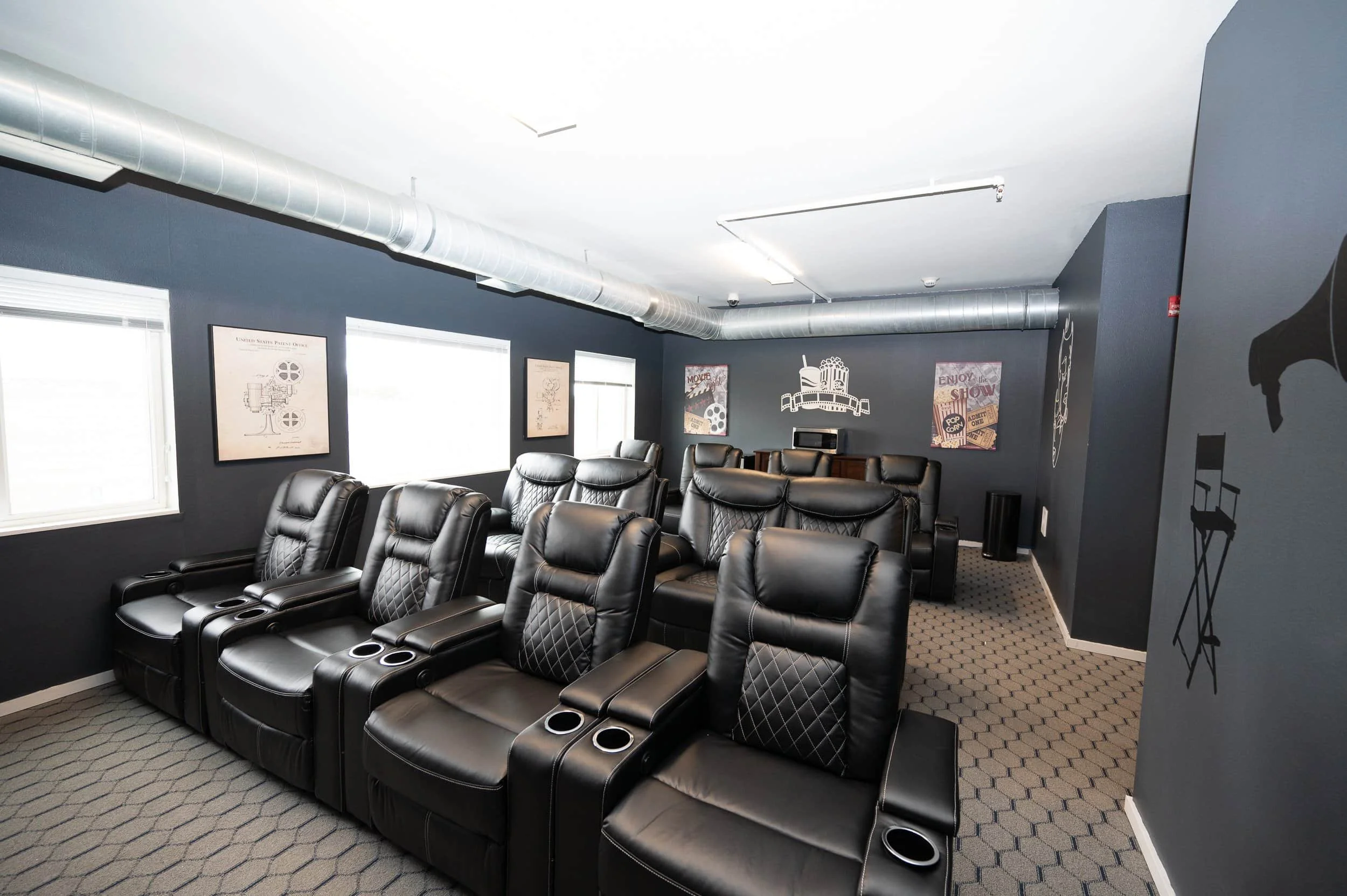Home theater room in apartments in Rochester with black leather recliners, gray walls, movie art, and natural light from windows.